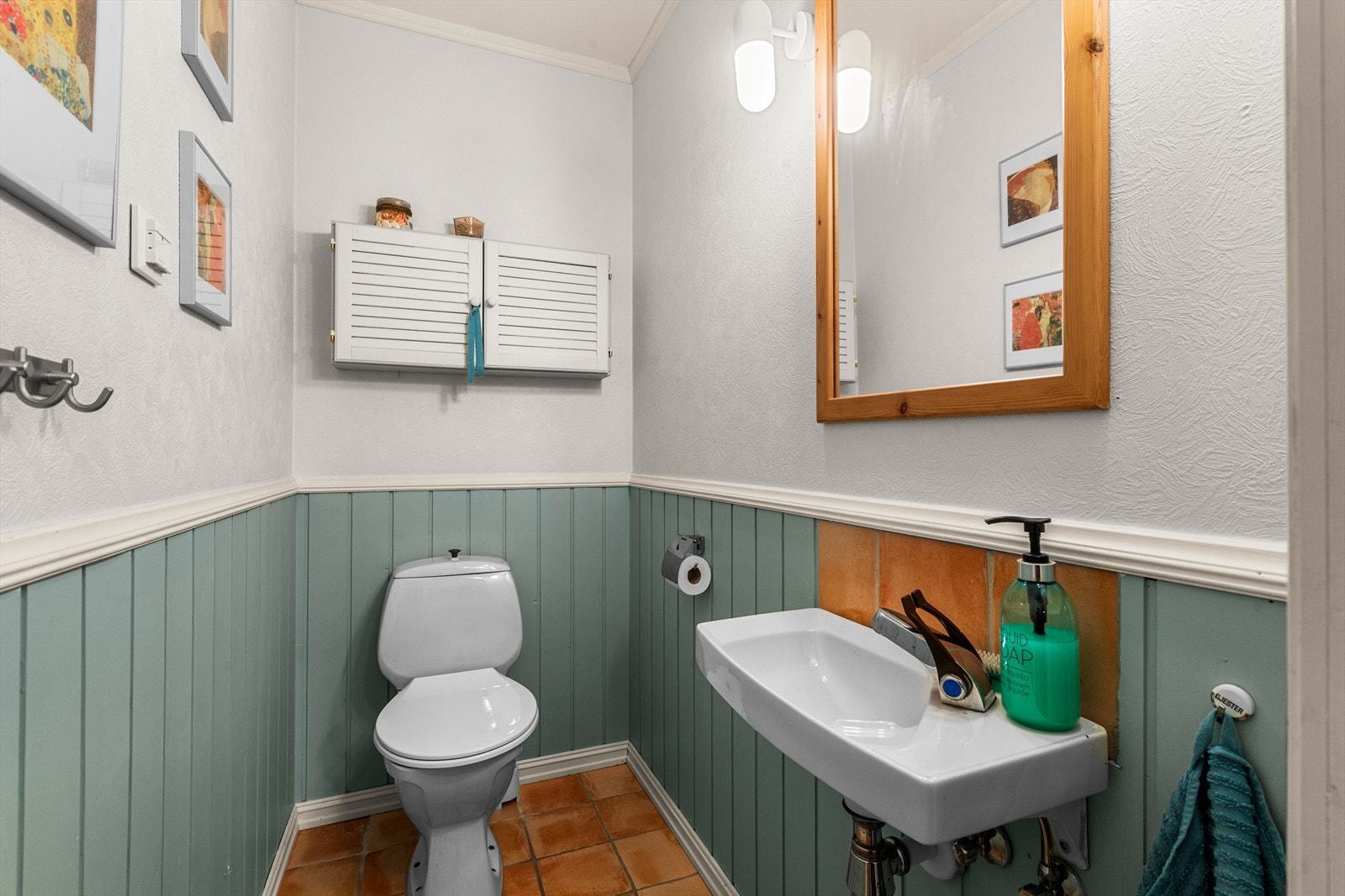 Flislagt gulv og halvpanel gir et klassisk uttrykk til gjestetoalettet. Speil med treinnramming og vegghengt skap gir praktisk oppbevaring. Galleribilde