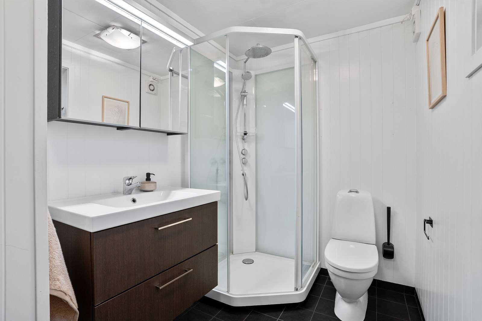 Badet har fliser på gulvet med varmekabler, samt et nyere dusjkabinett byttet av fagfolk i 2022 toalett, samt baderomsinnredning med speilskap over. Galleribilde