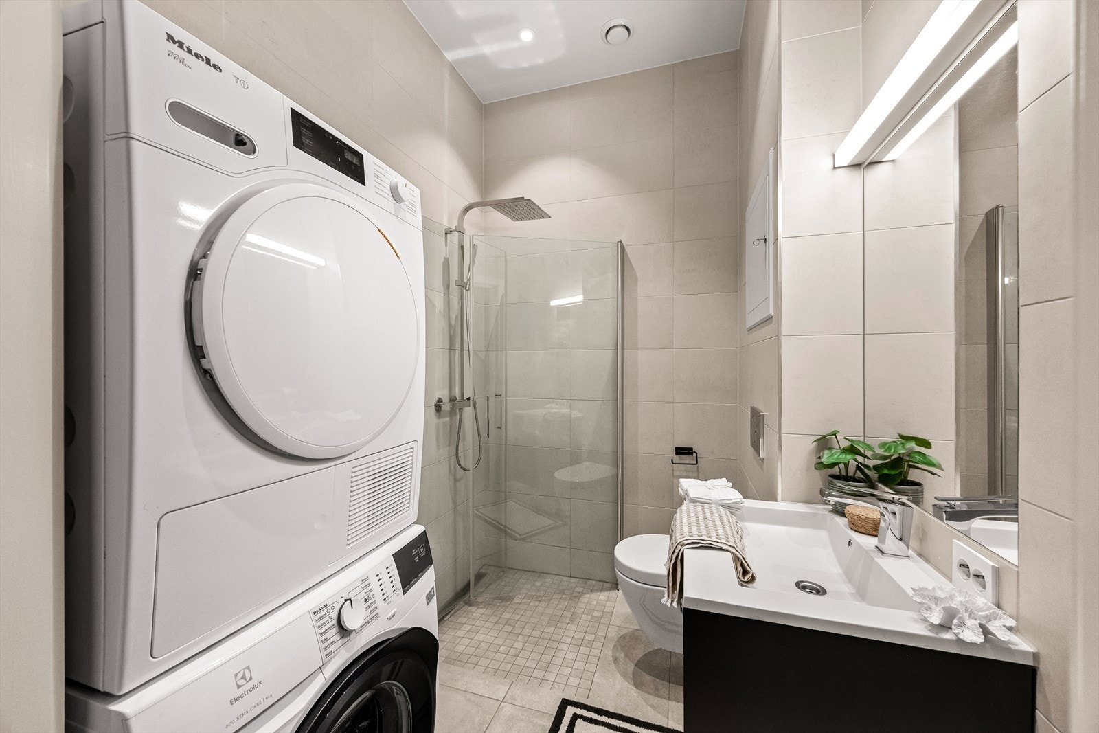 Badet er utstyrt med dusjhørne med regndusj og håndusj, opplegg for vaskemaskin/tørketrommel, servantskap, veggmontert wc, mekanisk avtrekk og rørfordelingsskap Galleribilde