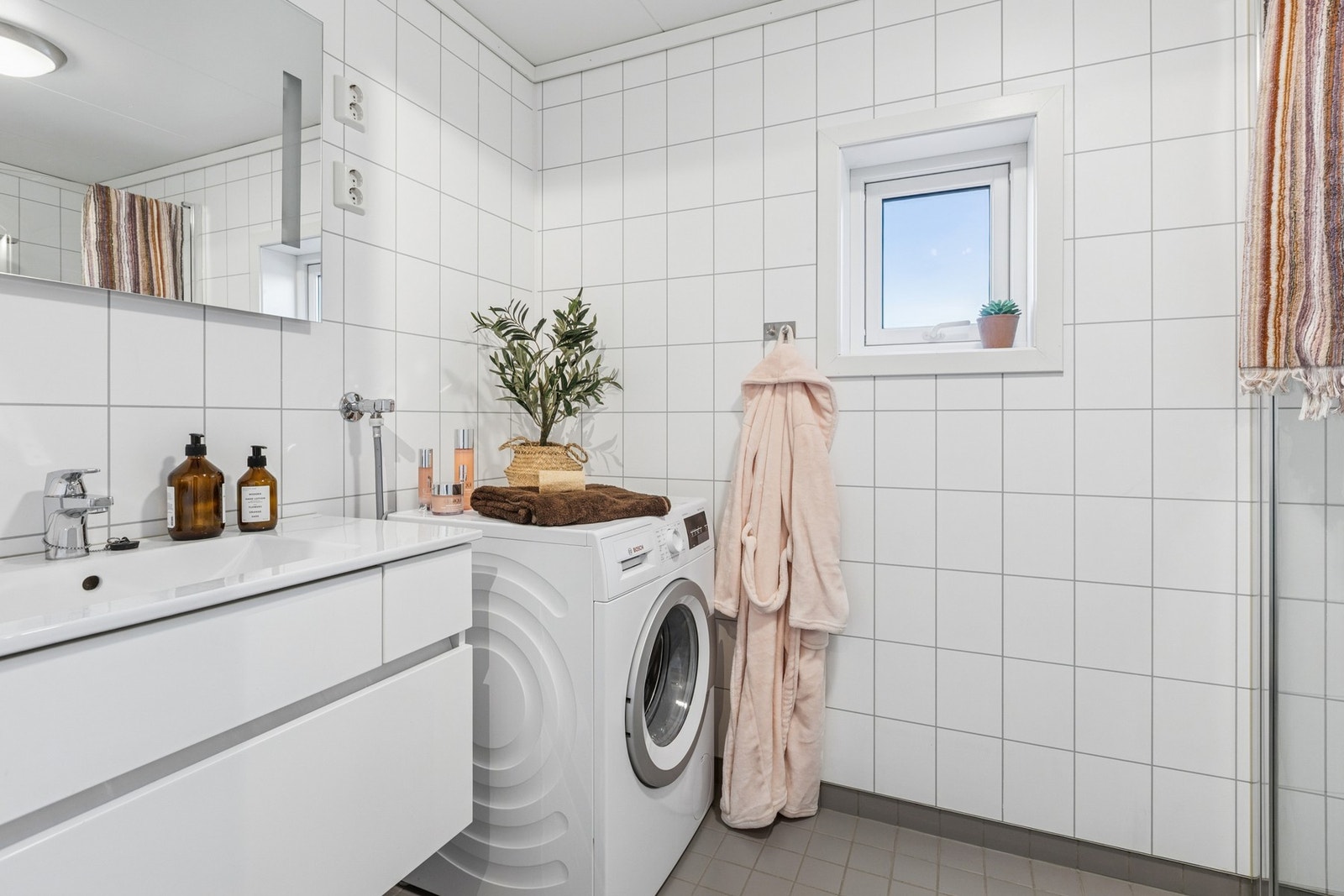 Badet har innsvingbare glassdører i dusjhjørnet, veggmontert wc og servant i skuffeseksjon samt speil med belysning. Galleribilde