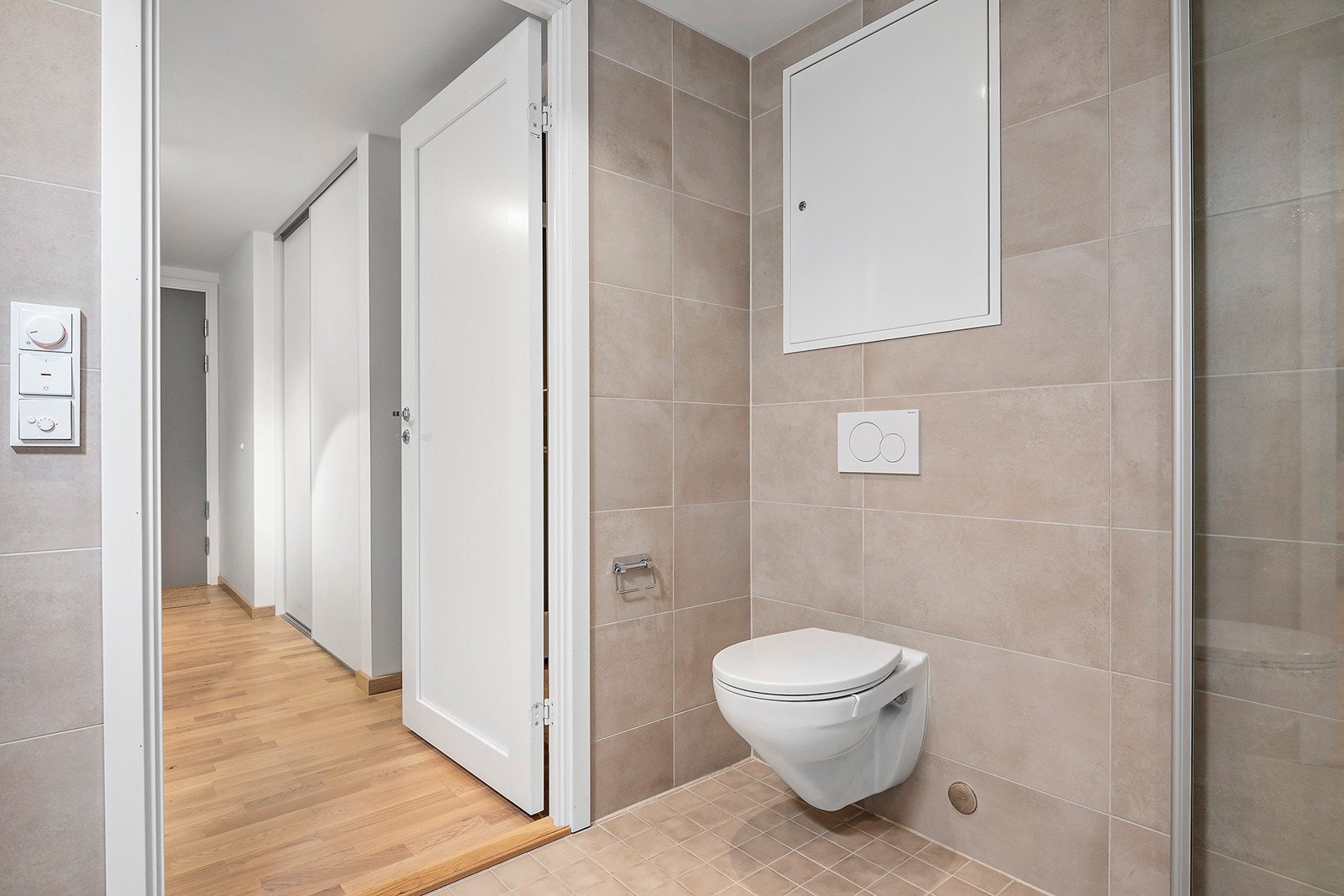 Badet er innredet med dusjhjørne, veggmontert WC, servant med skuffeseksjon, høyskap, speilskap med belysning samt opplegg for vaskemaskin. Galleribilde