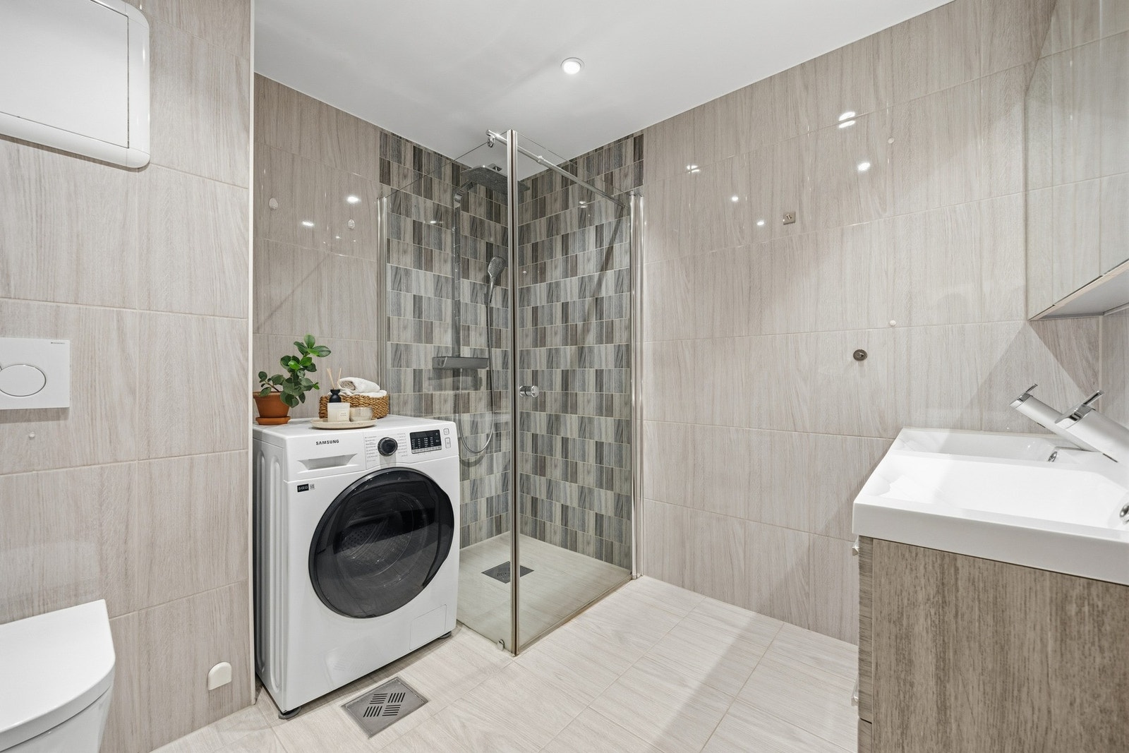 Stort, praktisk flislagt baderom med opplegg for vaskemaskin og tørketrommel. Galleribilde