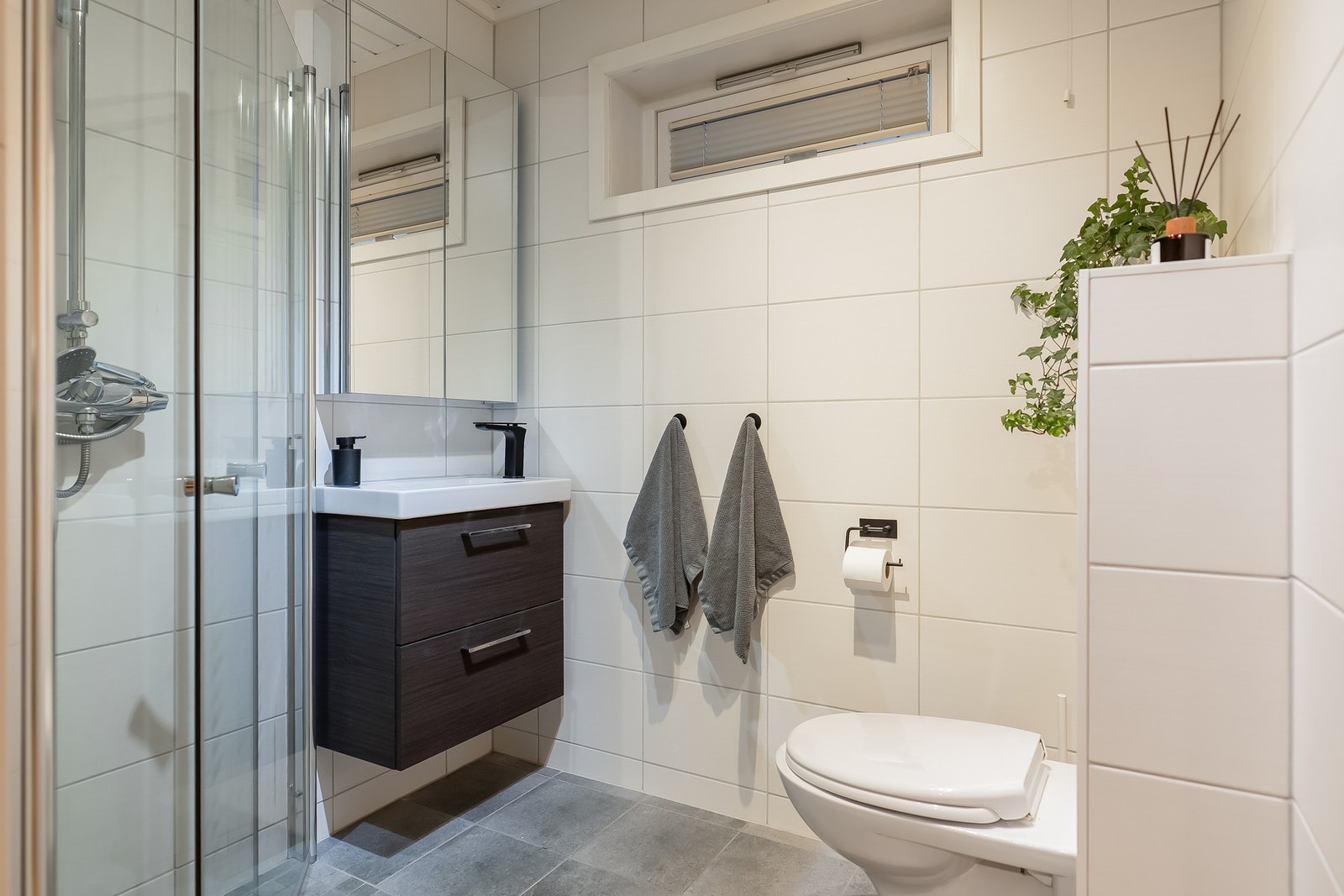 Bad i utleiedel, utstyrt med vegghengt toalett, servant med underskuffer og hjørnedusj. Galleribilde