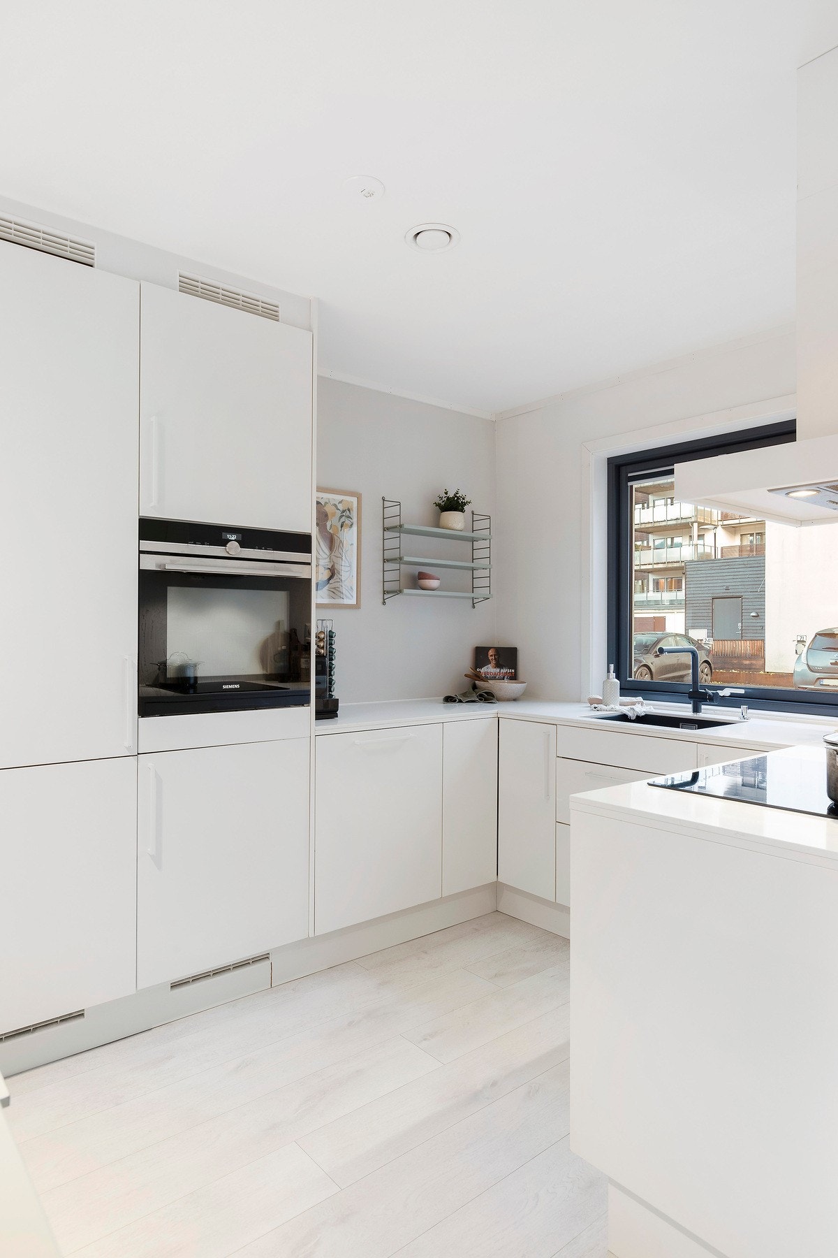 Kjøkkenet har en åpen og moderne løsning med slette fronter, benkeplate i komposittstein og integrerte hvitevarer Galleribilde