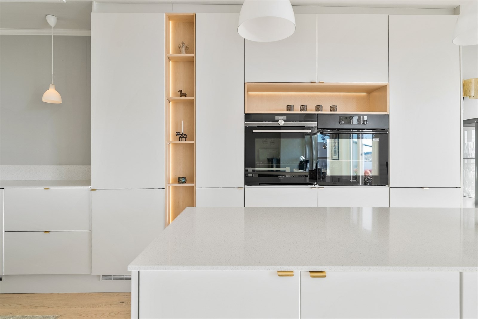 Uttrykket er lett og sømløst, med lyse, slette fronter, lys benkeplate i kompositt og lune detaljer i lyst tre og messing. Galleribilde