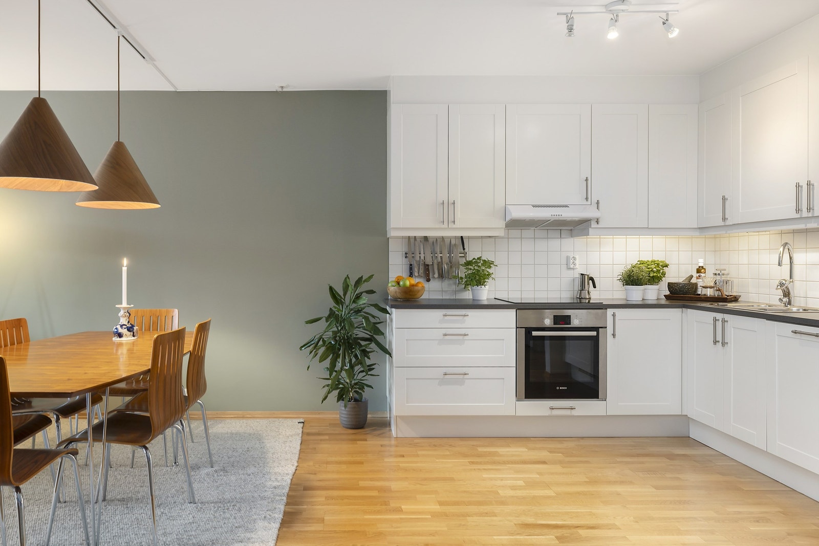 Åpen stue- og kjøkkenløsning med kjøkkeninnredning fra byggeår med glatte speilfronter og laminert benkeplate. Fliser mellom benkeplate og overskap. Galleribilde