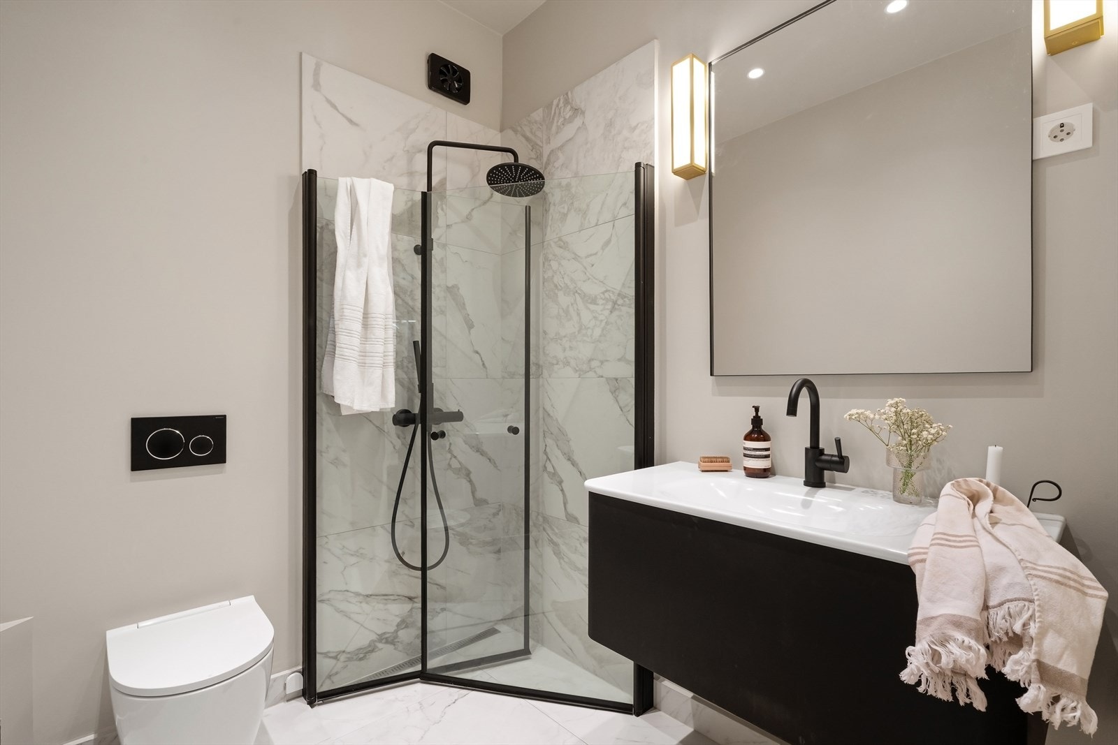 Delikat bad/vaskerom ved soverom pusset opp i 2021, med veggfestet toalett, dusj med innfellbare glassdører og marmorfliser fra Skógr Galleribilde
