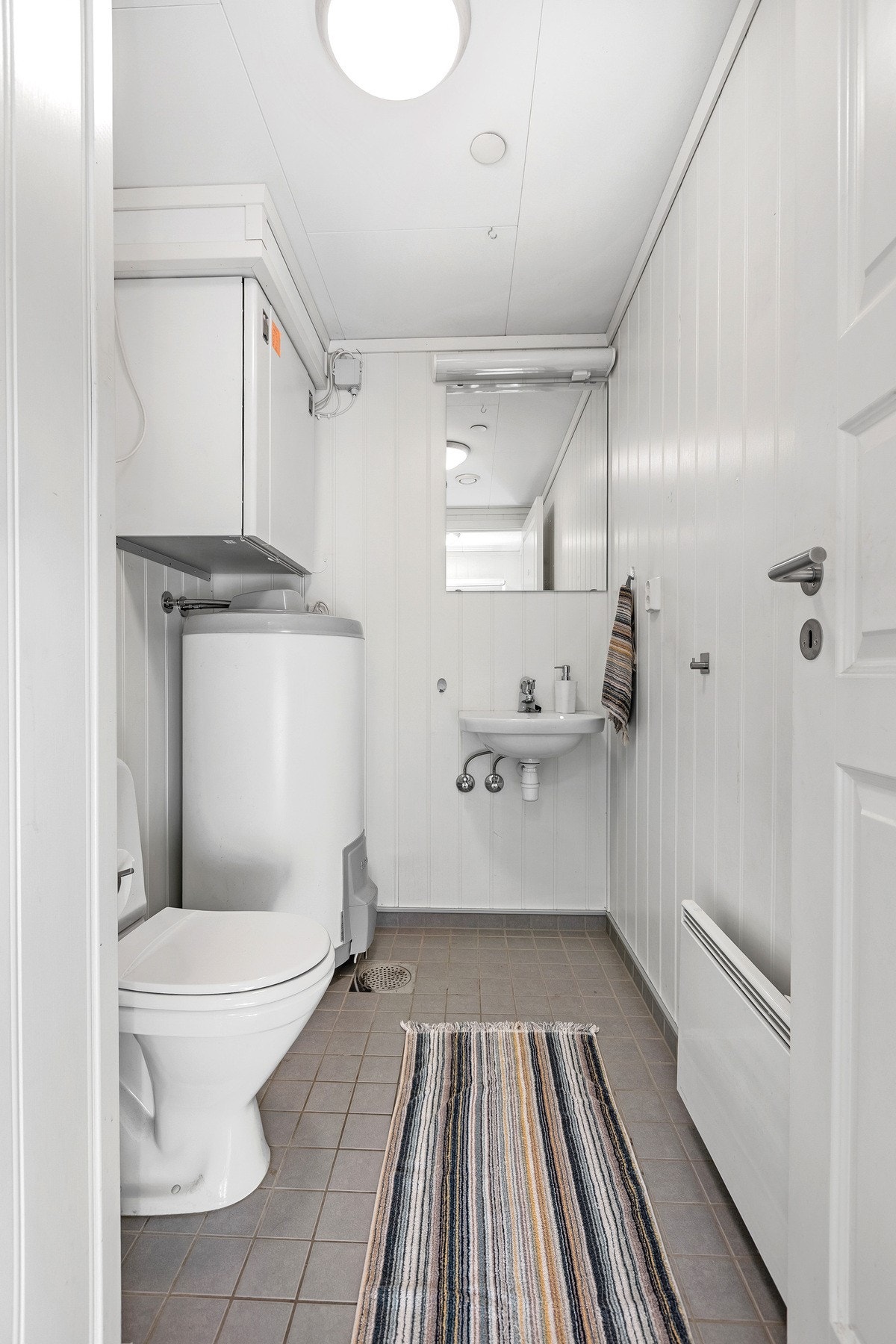 Toalettrommet har flislagt gulv med sluk og vegger med malte plater. Galleribilde