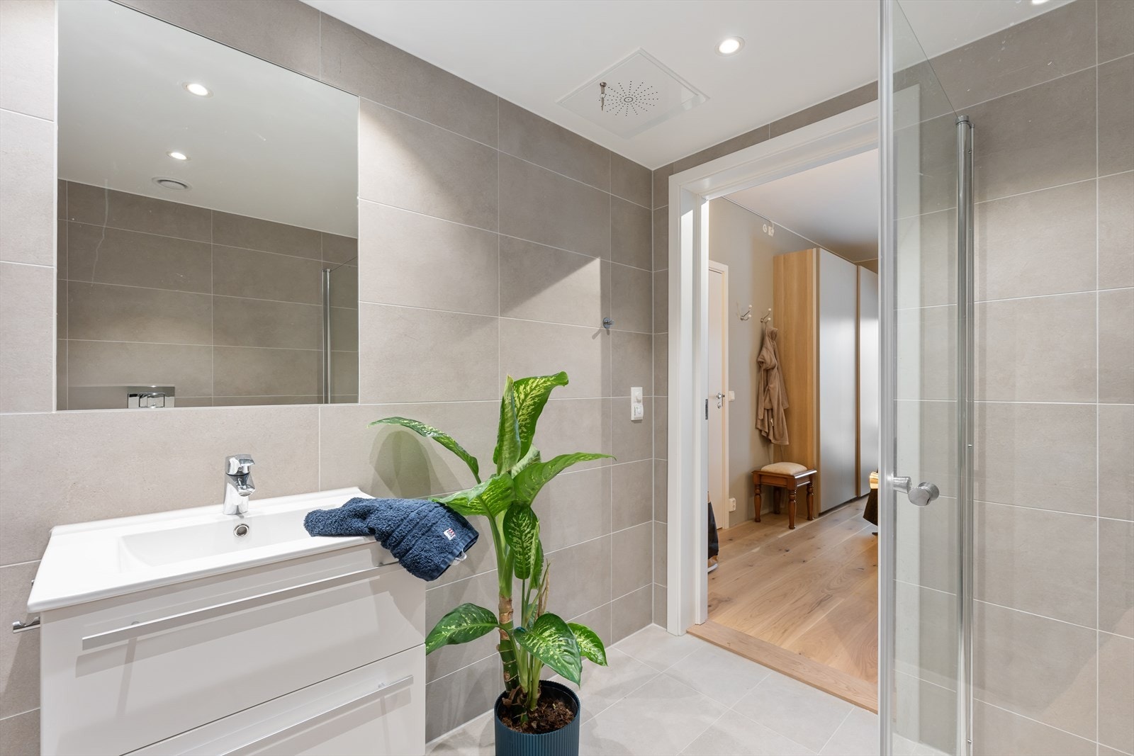 Badet er utstyrt med en moderne skuffeseksjon med heldekkende servant, speil, vegghengt toalett og dusjhjørne med glassdører. Galleribilde