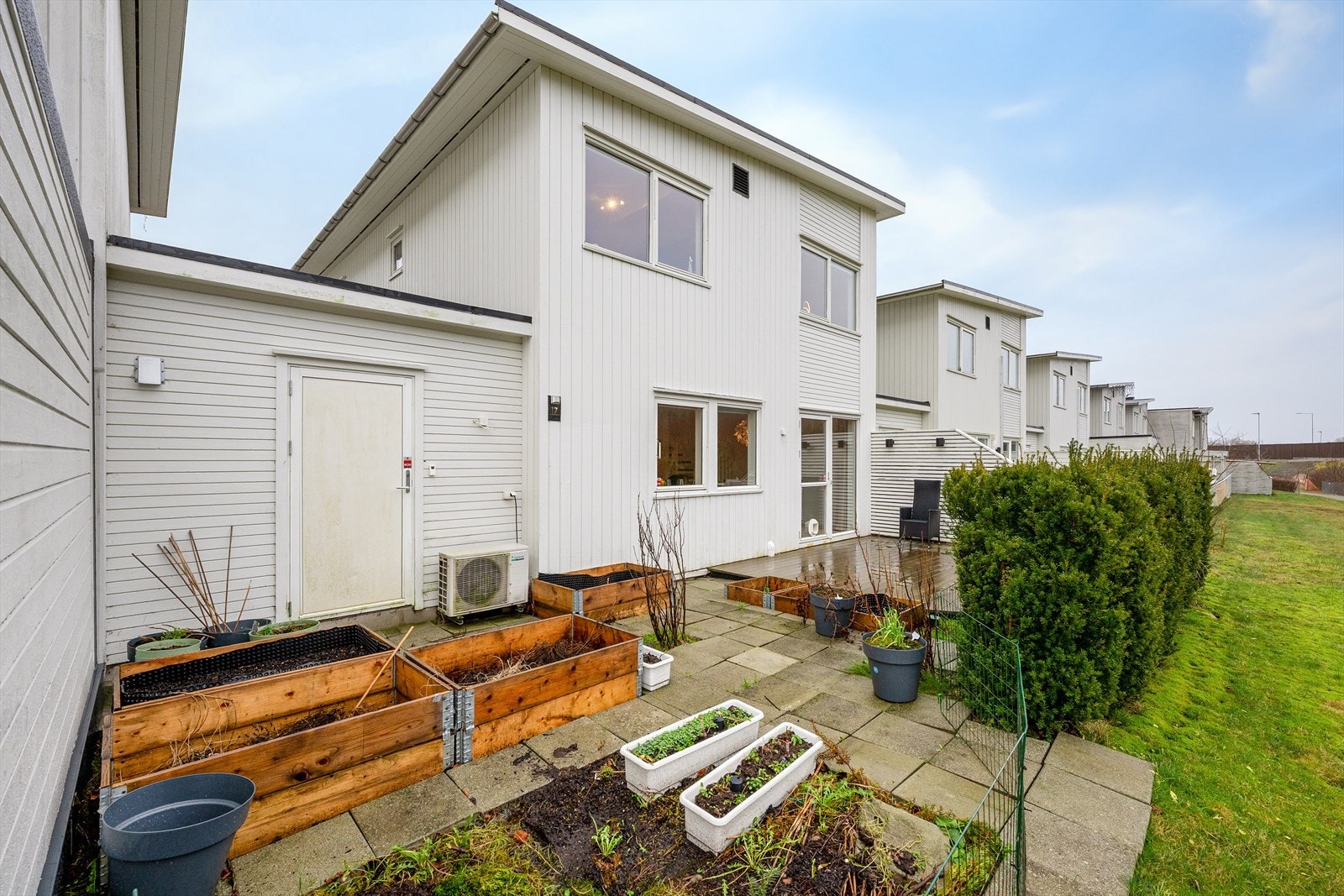 Romslig uteområde som er pent tilrettelagt med plantekasser, busker og terrasse. Galleribilde