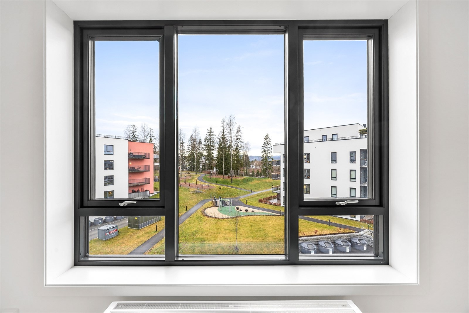 Fra vinduene ser man ut over velholdte grøntområder med lekeplass. Galleribilde