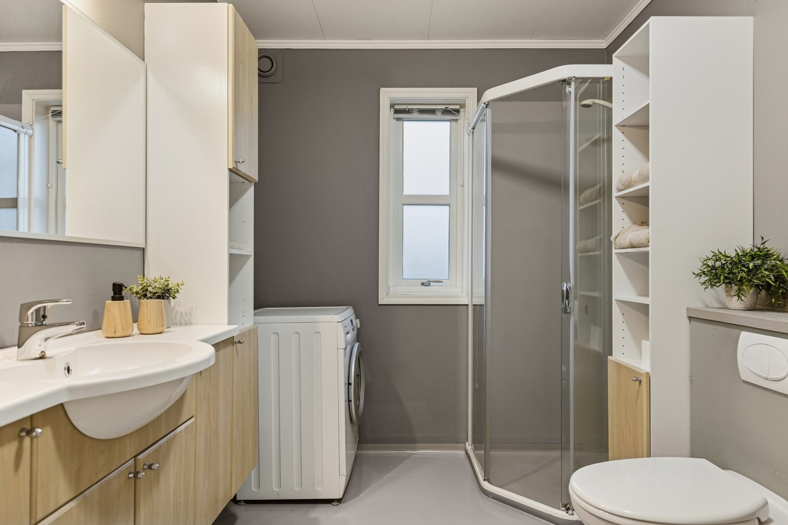 Bad i første etasje som er utstyrt med dusjnisje, vegghengt toalett og servant med god skapplass. Det er opplegg for vaskemaskin. Rommet har malte flater med grå vegger og lyst gulv. Det er også en varmtvannsbereder på ca 200 liter. Galleribilde