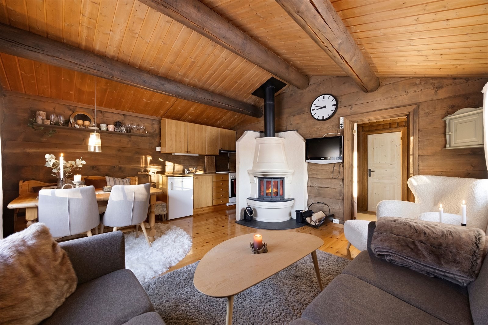 Åpen stue- og kjøkkenløsning med en imponerende peisovn som skaper en varm og innbydende atmosfære. Galleribilde