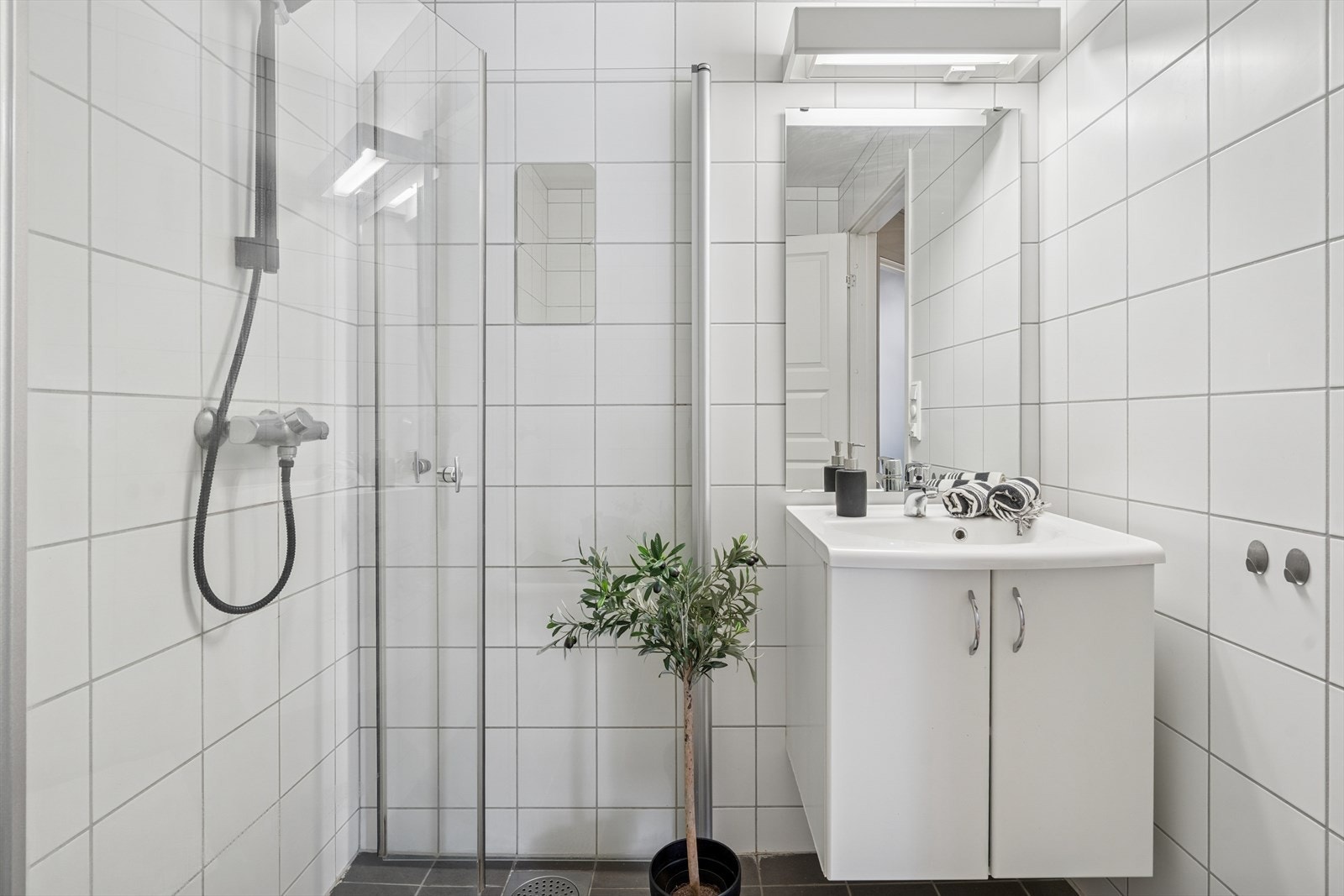 Baderommet er innredet med nedfelt servant, veggmontert toalett, dusjhjørne med innfellbare dusjdører og opplegg for vaskemaskin. Galleribilde