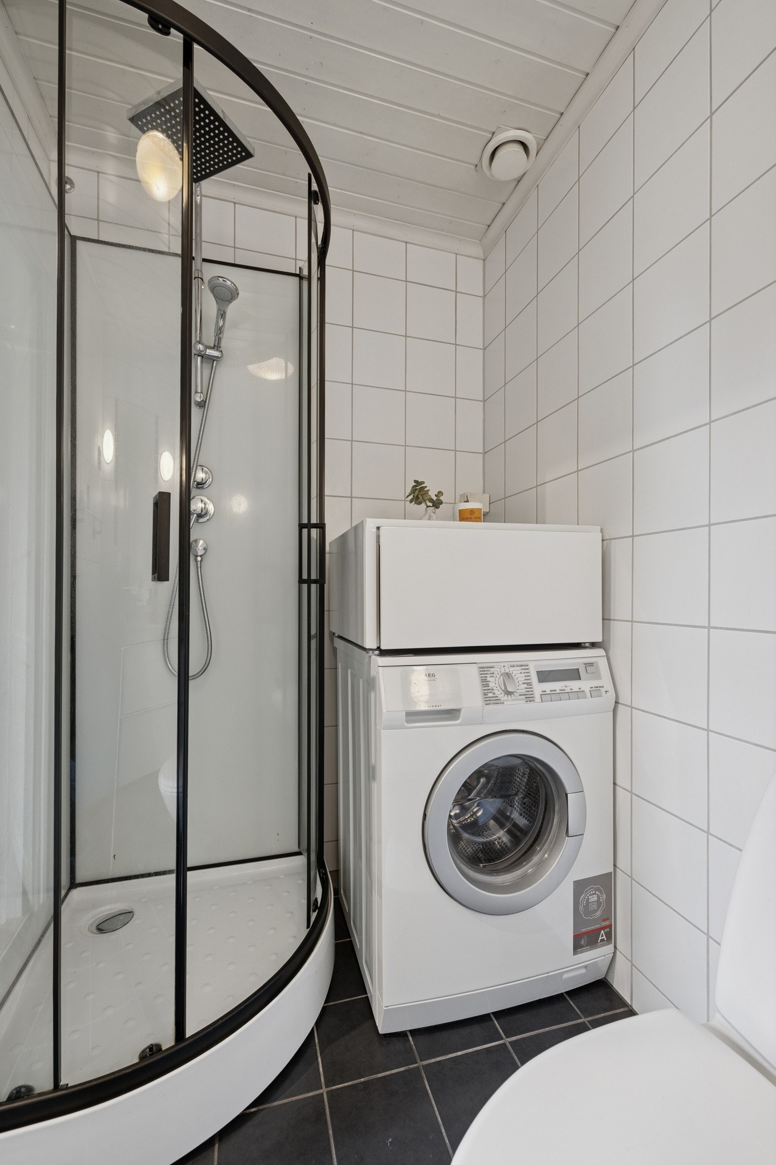 Lyst og praktisk baderom med dusjkabinett og opplegg for vaskemaskin. Galleribilde