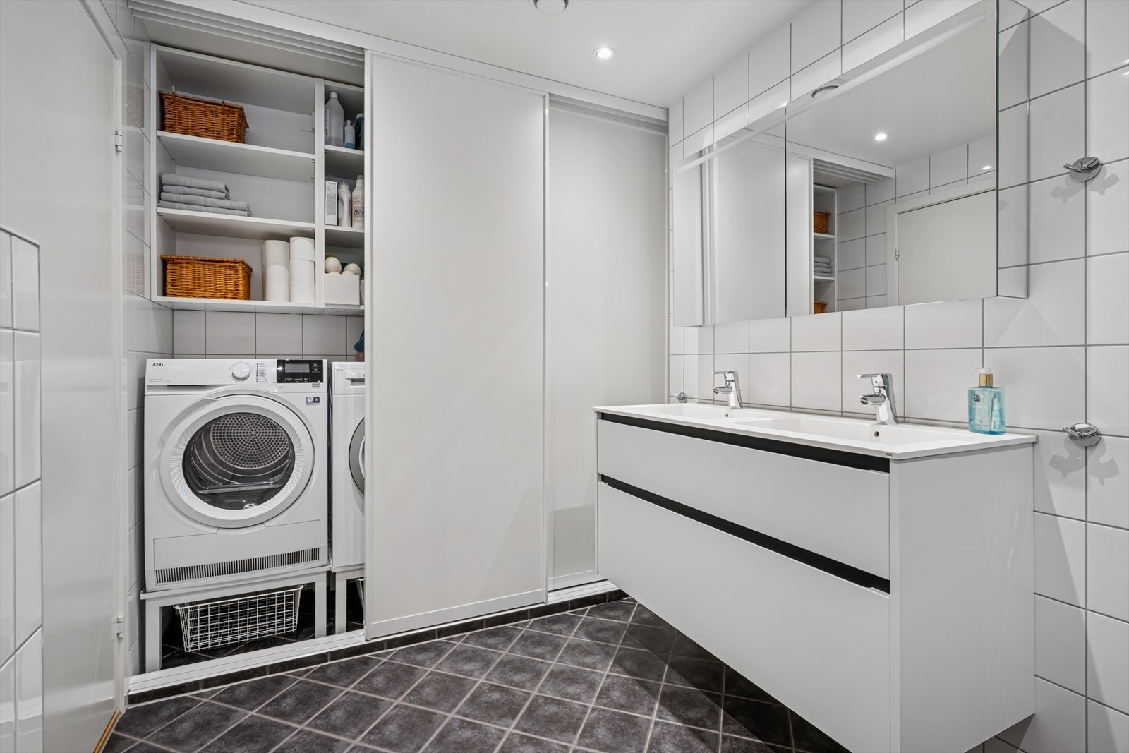 Badet er innredet med servantskap med nedfelt servant, veggmontert toalett og dusjhjørne med dusjvegger. Det er også opplegg for vaskemaskin som er skjult bak skyvedører. Galleribilde