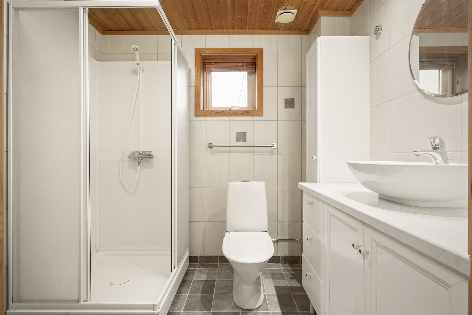 Baderom med flislagte gulv og vegger, samt varmekabler i gulv. Innredningen består av servant, høyskap, toalett, dusjkabinett og opplegg for vaskemaskin. Galleribilde