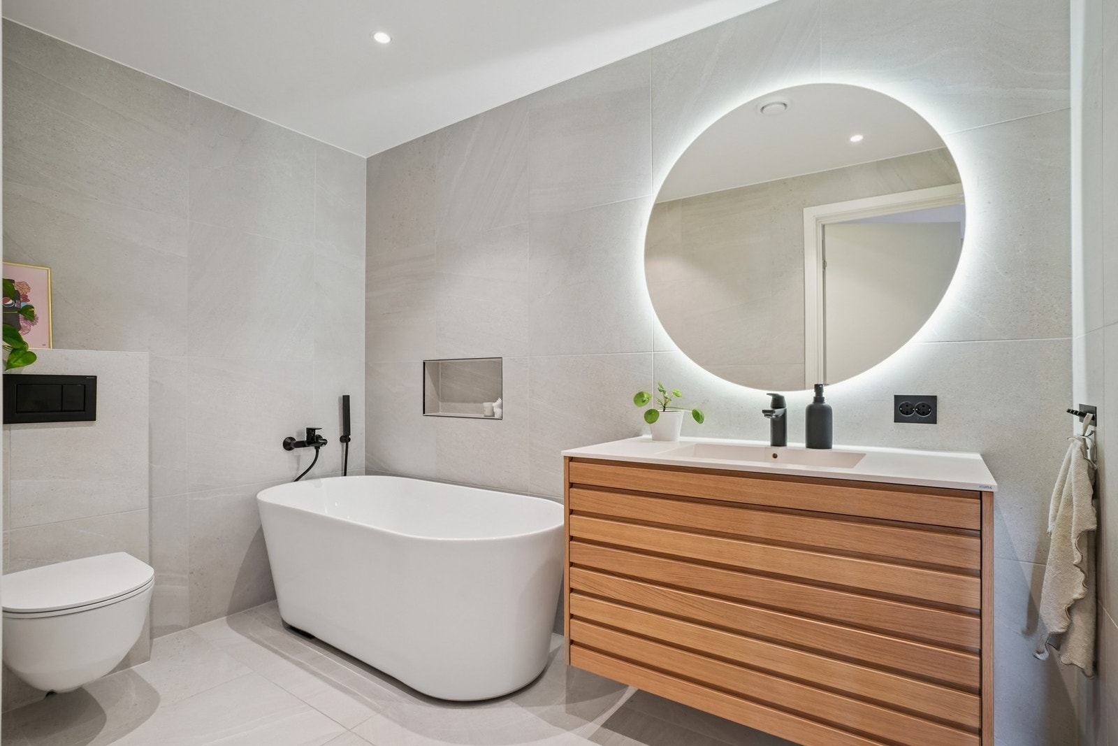 Her er det utstyrt med et flott baderomsmøbel med overliggende speil med belysning, vegghengt toalett og badekar. Legg merke til nisjen ved badekaret. Galleribilde