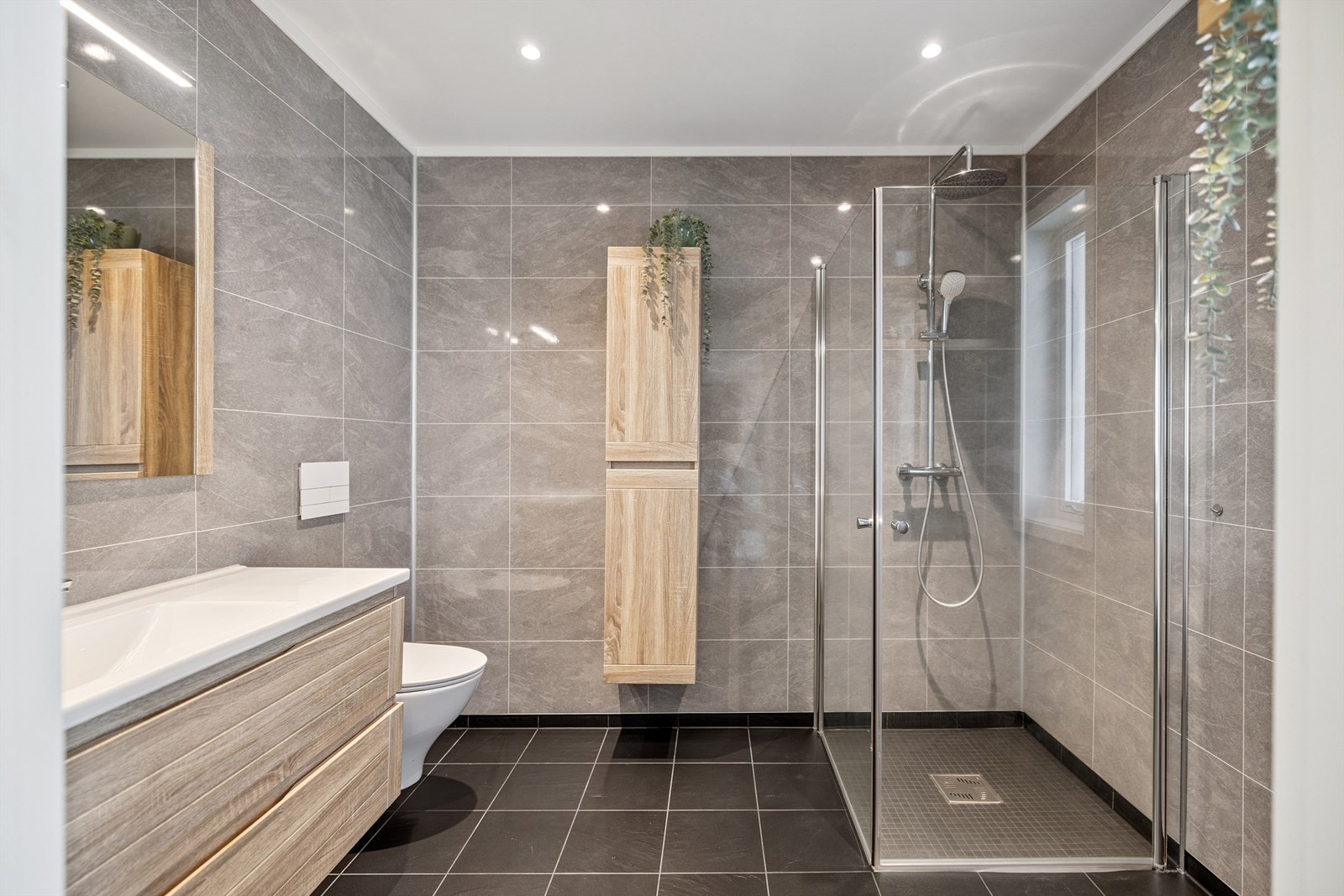 Pent bad utstyrt med dusjhjørne med glassdører og vegghengt toalett. Galleribilde