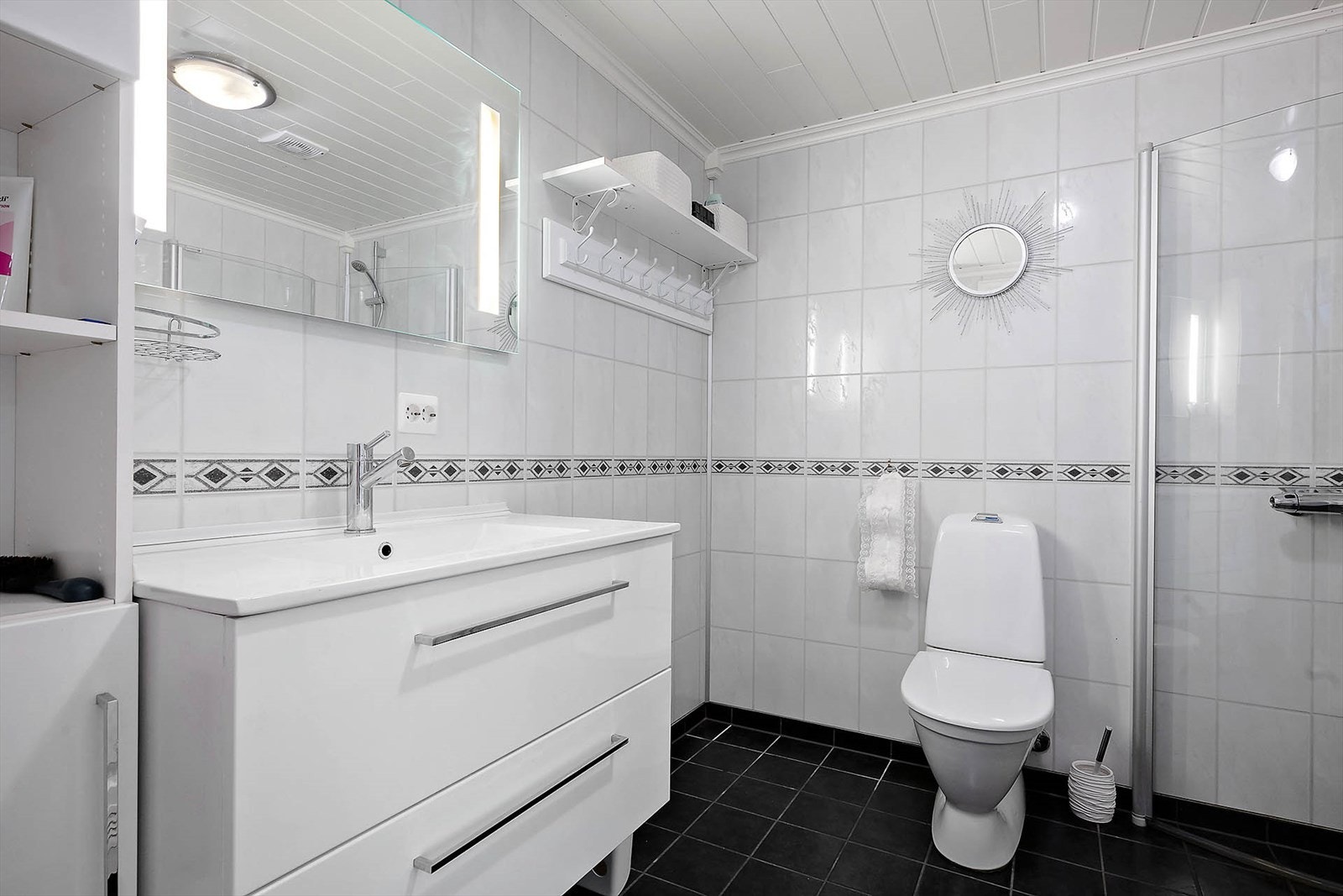 Badet er av lyse farger og har flislagt gulv med varmekabler og vegger med baderomsplater. Badet er har opplegg for vaskemaskin og tørketrommel. Galleribilde