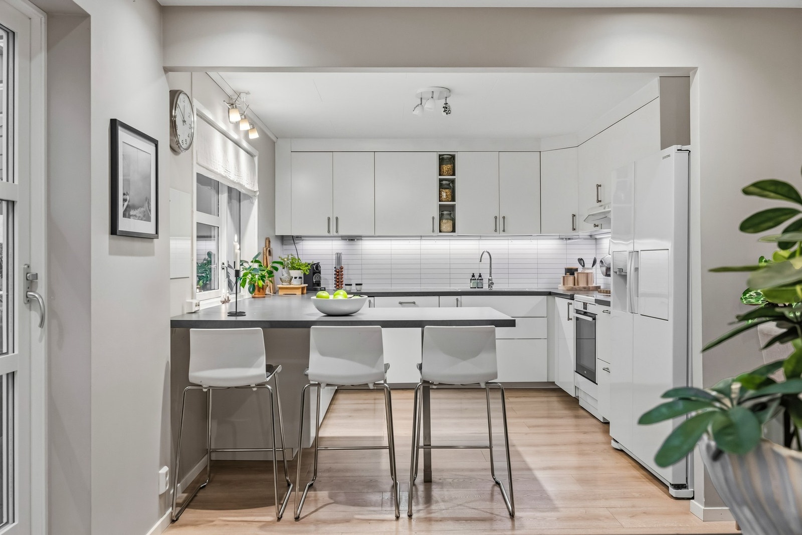 Lyst og pent kjøkken med hvite, glatte fronter og mørk benkeplate Galleribilde