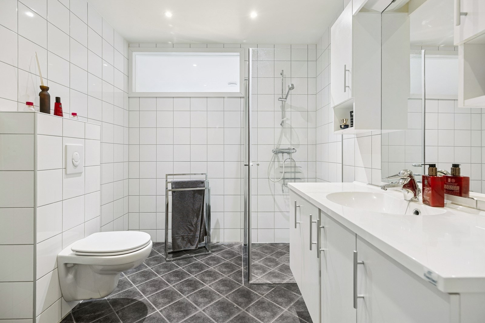 Badet er innredet med servantskap med nedfelt servant, veggmontert toalett og dusjhjørne med dusjvegger. Galleribilde