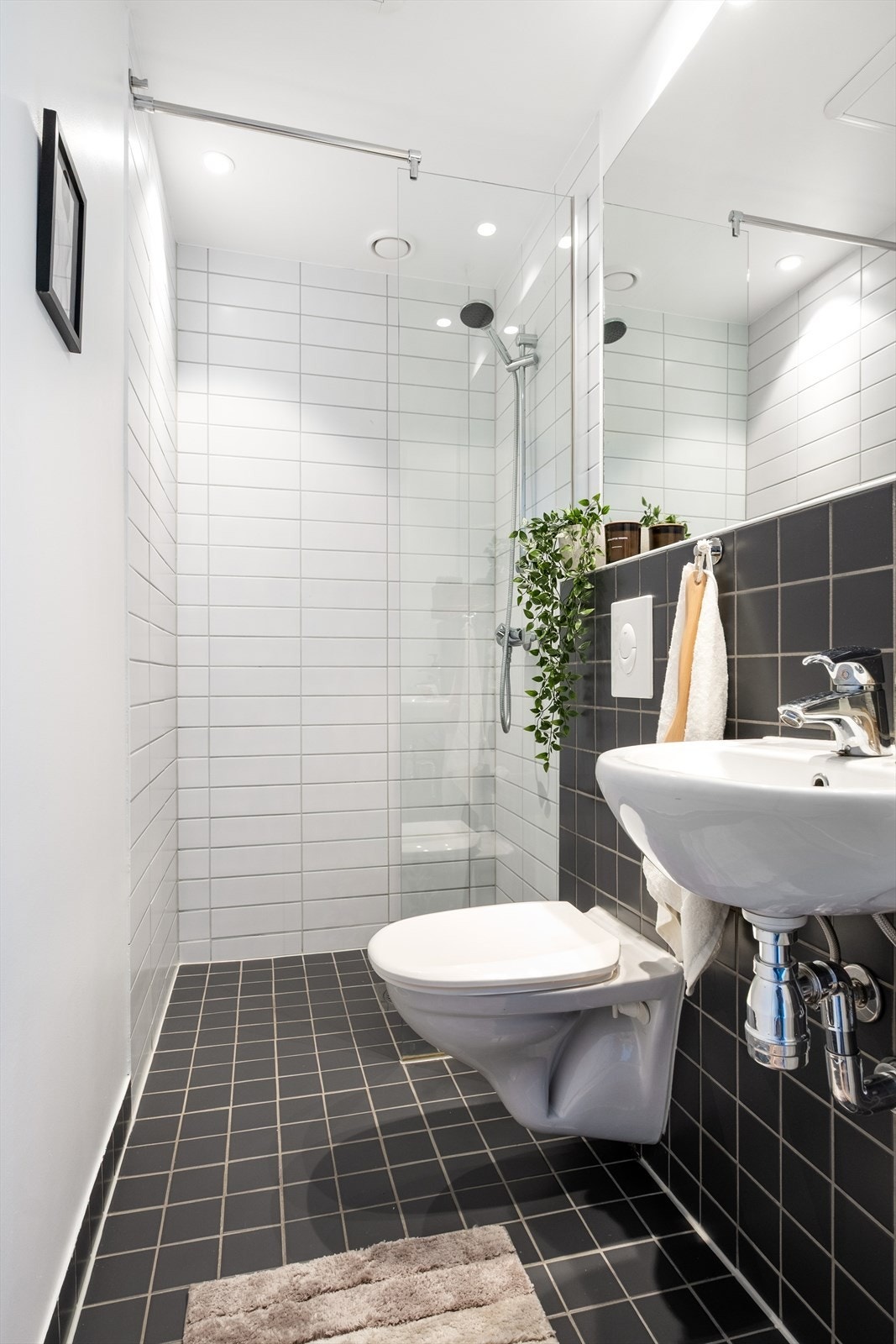 Baderom med flislagt gulv, varmekabler, fliser og malte flater på vegger, avtrekk, speil, downlights, servant, dusj hjørne med glassvegg, vegghengt toalett. Galleribilde