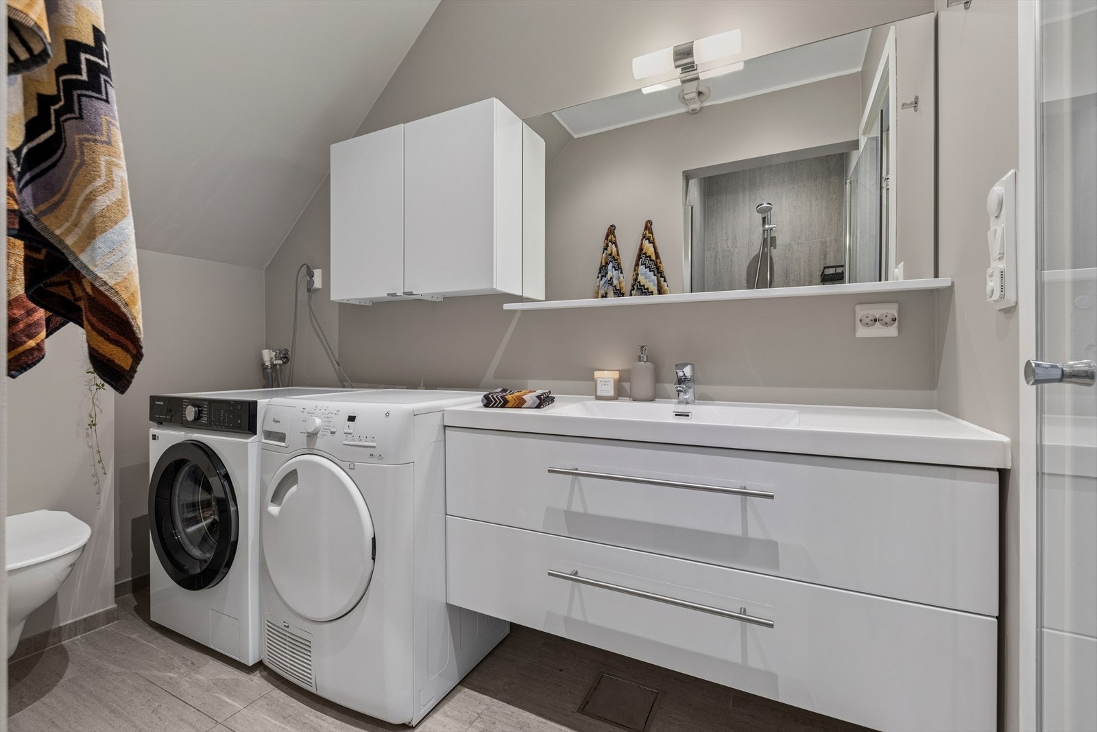 Badet er ellers utstyrt med dusjnisje, vegghengt toalett og baderomsinnredning med nedfelt servant. I tillegg har man opplegg for vaskemaskin og plass til tørketrommel. Galleribilde