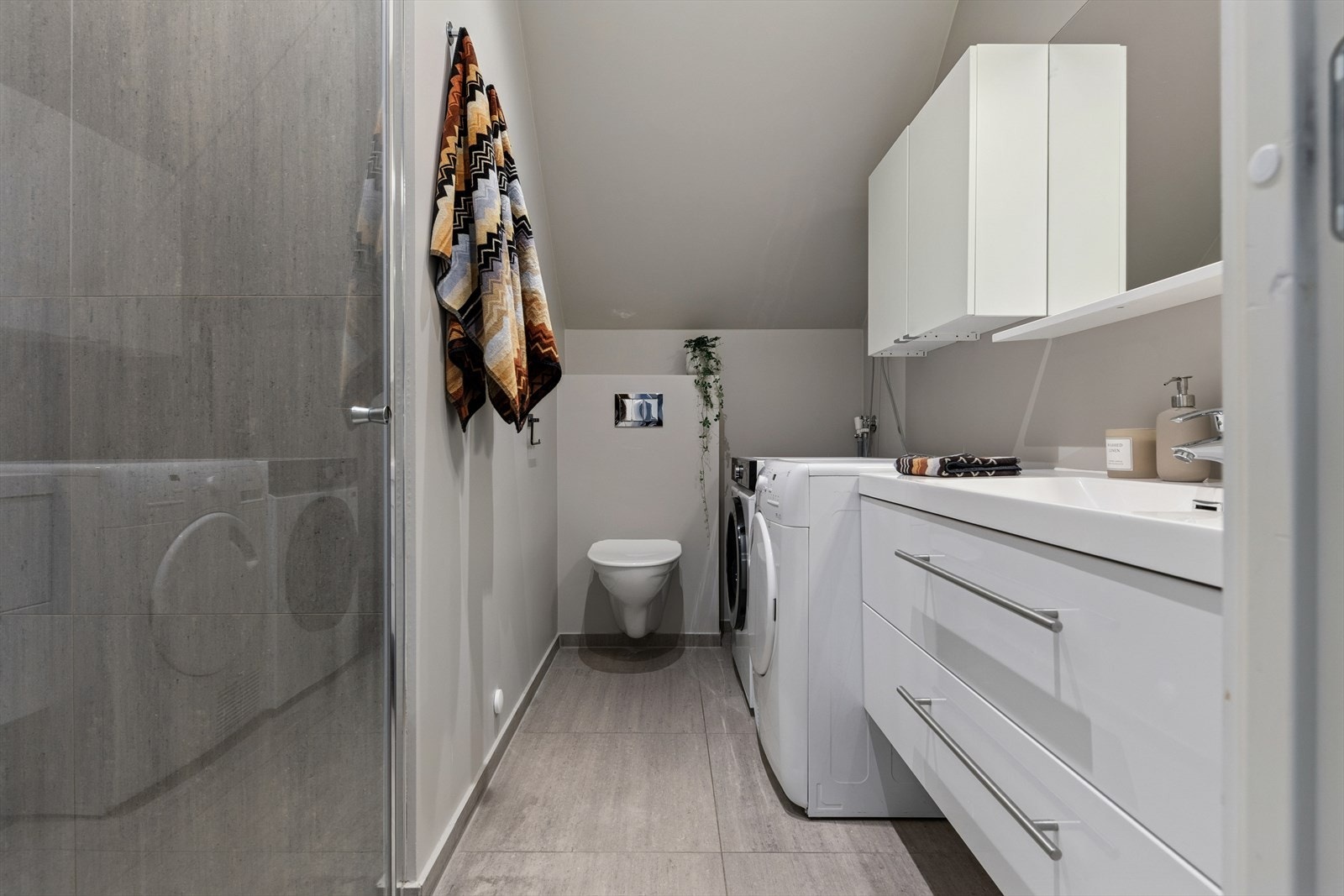 Baderommet ble pusset opp i 2017 og er tidløst innredet med grå fliser på gulv og i dusjsone og ellers malte flater. I gulvet har man også varmekabler for ekstra komfort. Galleribilde