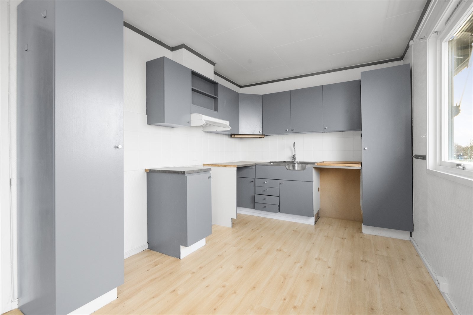 Kjøkkenet har eldre kjøkkeninnredning med malte fronter og flis på vegg over laminat benkeplate. Heltrukket benkebeslag i rustfritt stål. Galleribilde