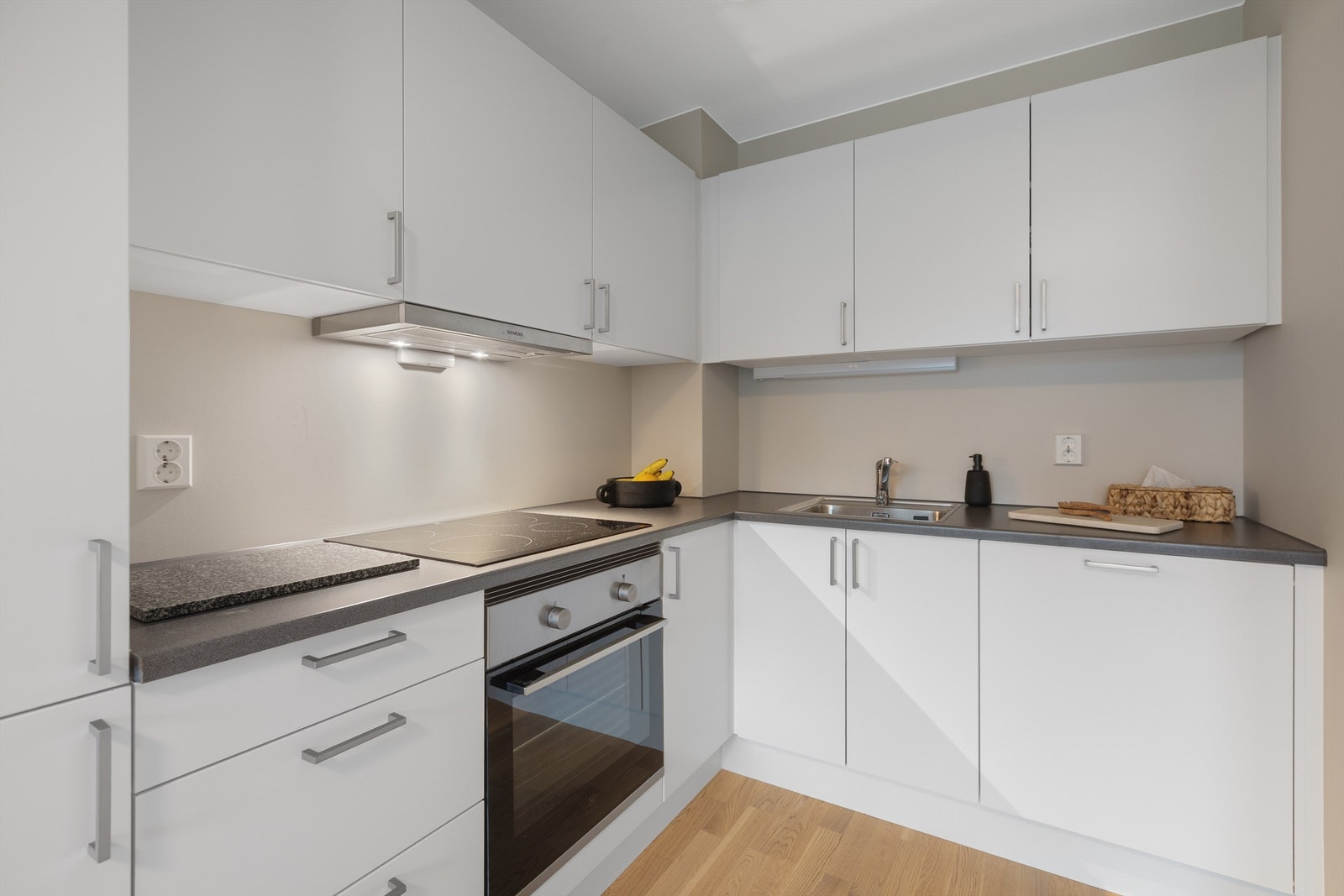 Kjøkken med nedfelt oppvaskkum med ett-greps kjøkkenarmatur, integrert stekeovn og platetopp, ventilator i overskap Galleribilde