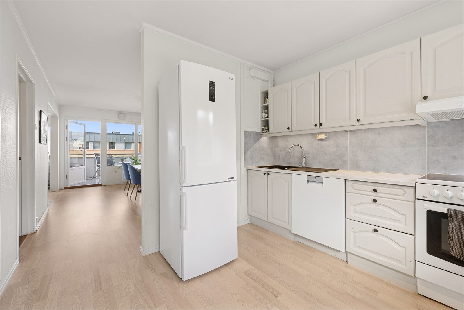 Kjøkkeninnredningen har hvite, profilerte fronter og lys laminert benkeplate med nedfelt kjøkkenkum. Galleribilde