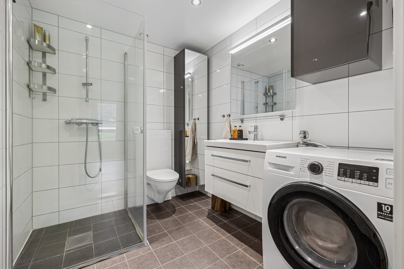 Delikat flislagt bad/vaskerom med elektriske varmekabler i gulv og downlights i himling. Rommet er utstyrt med nedfelt servant, høyskap med speil, veggmontert toalett og dusjvegger/hjørne. Opplegg for vaskemaskin. Balansert ventilasjon. Galleribilde