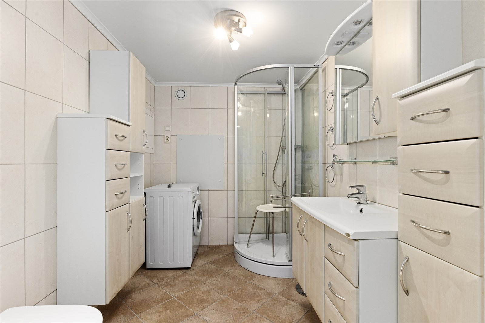 Pent bad med flis på gulv og vegger oppgradert av borettslaget i 2012. Her er det vegghengt toalett, dusjkabinett og en romslig innredning med heldekkende hvit vask, slette fronter og speil. Galleribilde