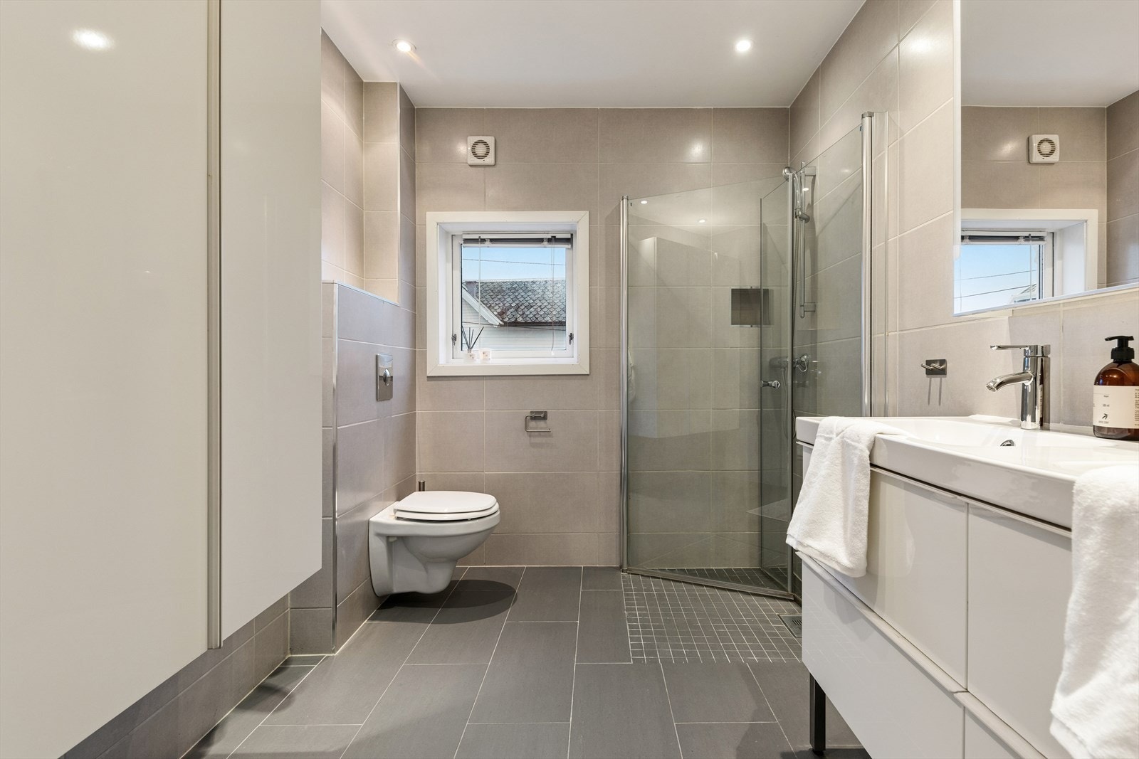 Badet er innredet med veggmontert totalett, dusj med glassdør fra 2022, baderomsinnredning med dobbel servant, speilskap, samt veggskap. Galleribilde