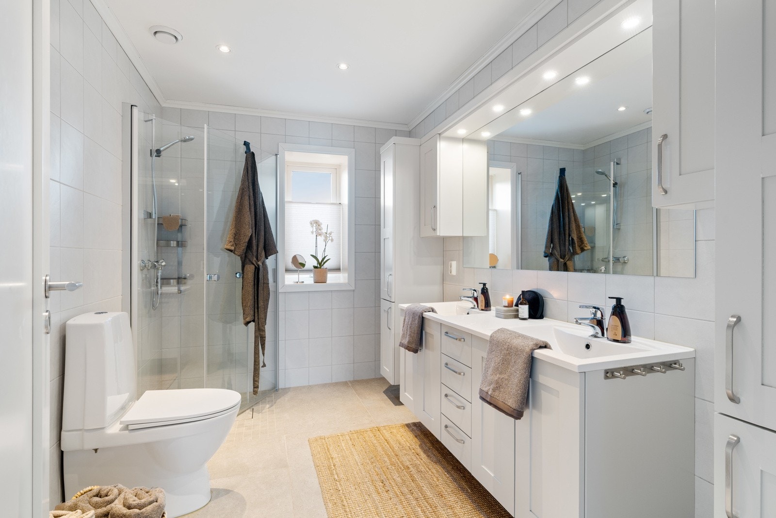 Lyst og elegant flislagt baderom på 6,5 kvm med toalett, dusjhjørnet, dobbelservant med underbygg og rikelig oppbevaringsplass i skap. Galleribilde