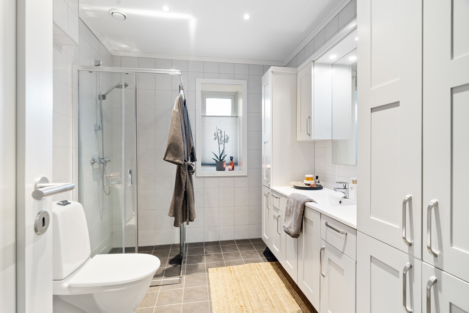 Romslig og lekkert flislagt baderom på 7 kvm, velutstyrt med toalett, dusjhjørnet, servant med underbygg og rikelig med oppbevaringsplass i skap. Galleribilde