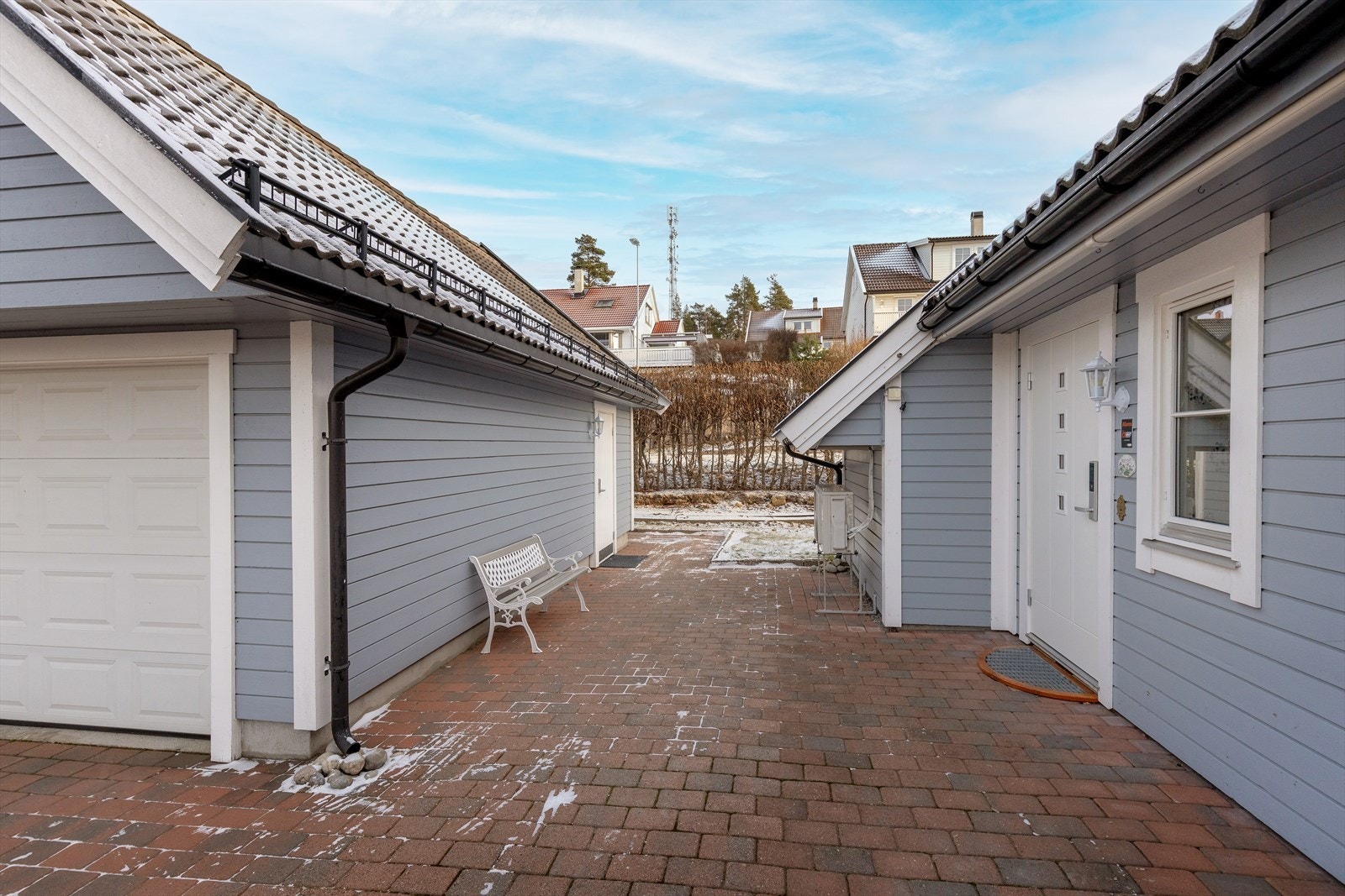 Det steinbelagte tunet mellom boligen og garasjen skaper et helhetlig og innbydende inngangsparti. Galleribilde