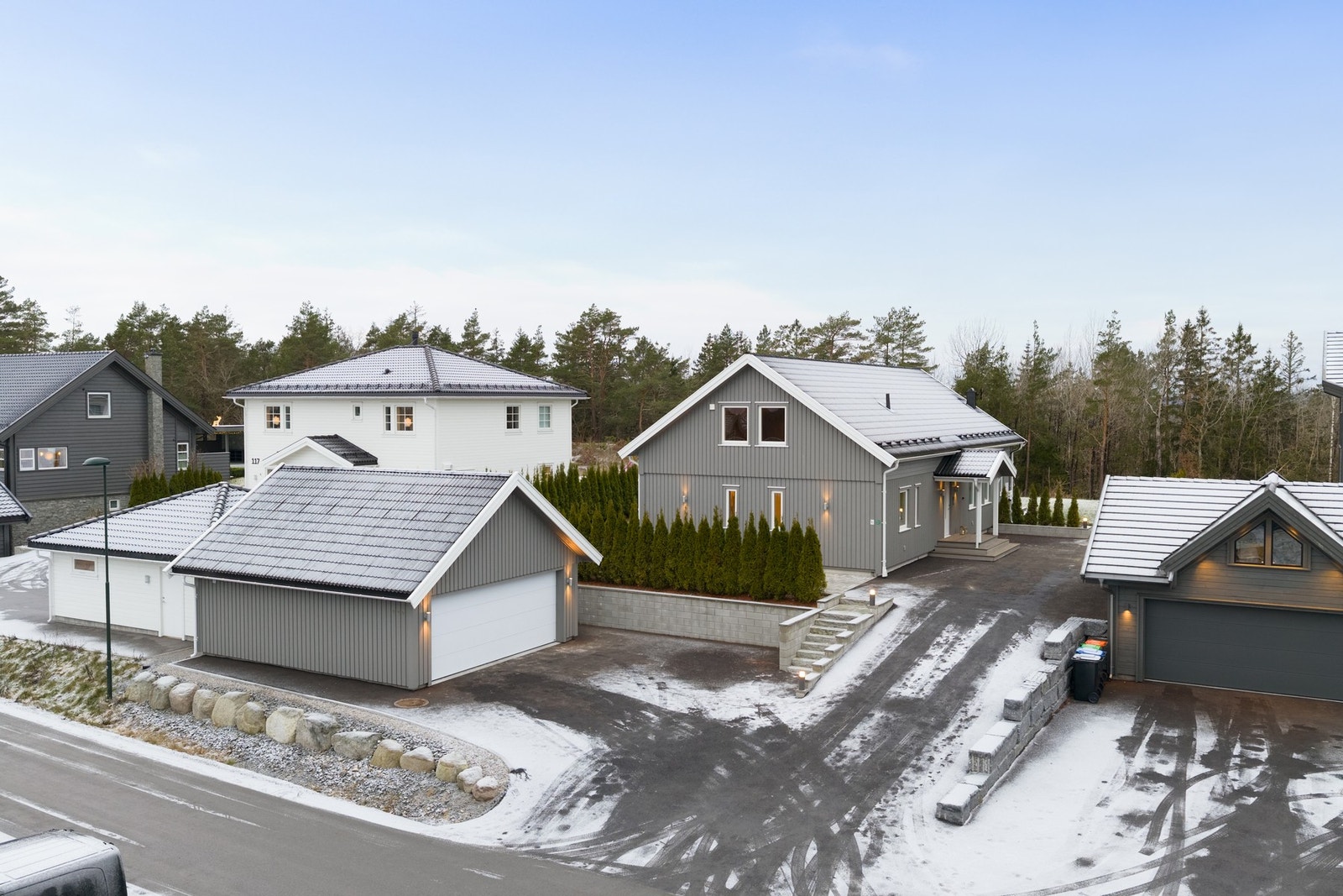 Oversiktsbilde av eiendommen sett fra Torpeveien. Huset ligger i blindvei, det grenser mot skog, så her er det lett å finne roen. Dobbelgarasje med elbillader. Galleribilde