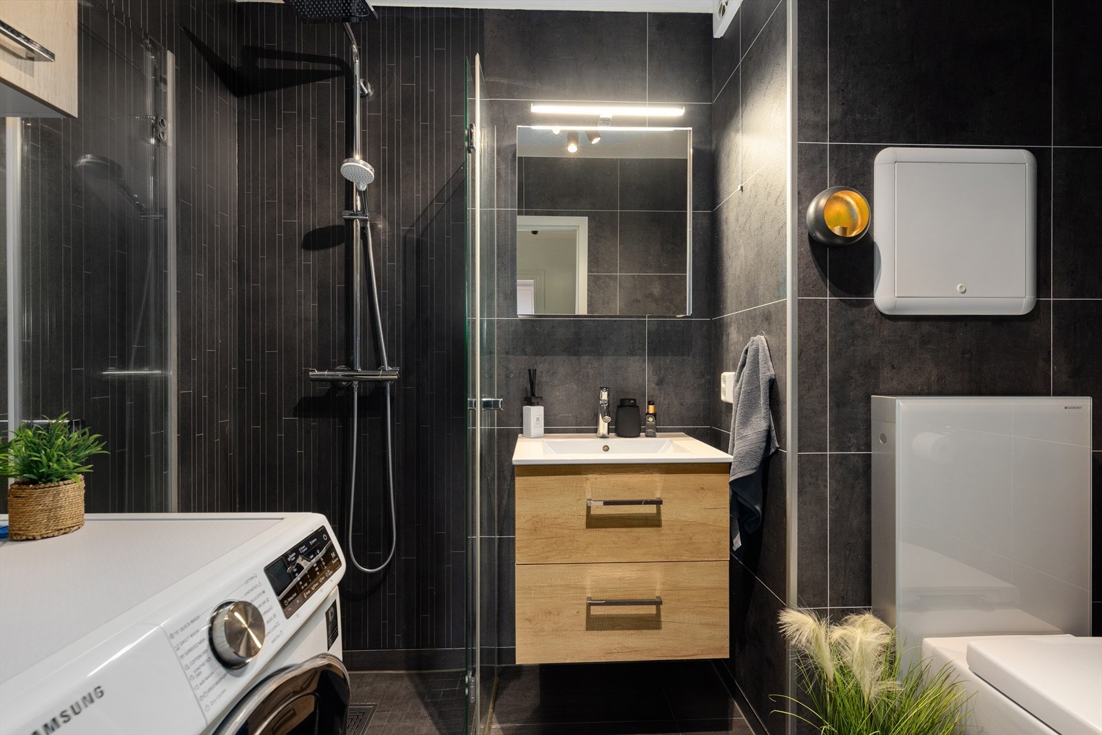 Delikat, flislagt bad renovert i 2022. Badet har elektriske varmekabler i gulv og er utstyrt med veggmontert toalett, dusj med dusvegg og opplegg for vaskemaskin. Galleribilde