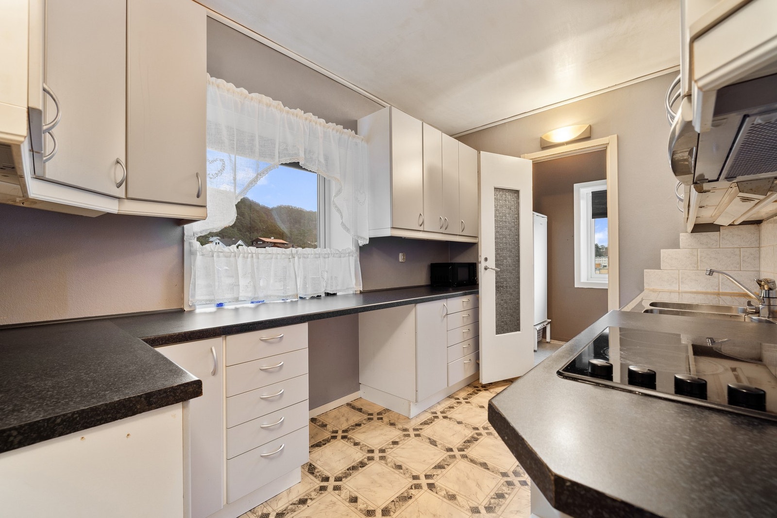 Hvit kjøkkeninnredning med glatte fronter og benkeplate i lamint. Galleribilde