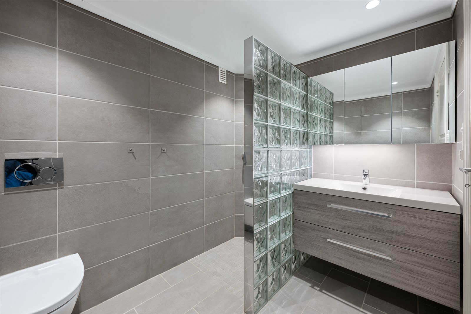 Rålekkert flislagt bad med stilig dusjnisje, vegghengt wc og stor baderomsinnredning. Galleribilde