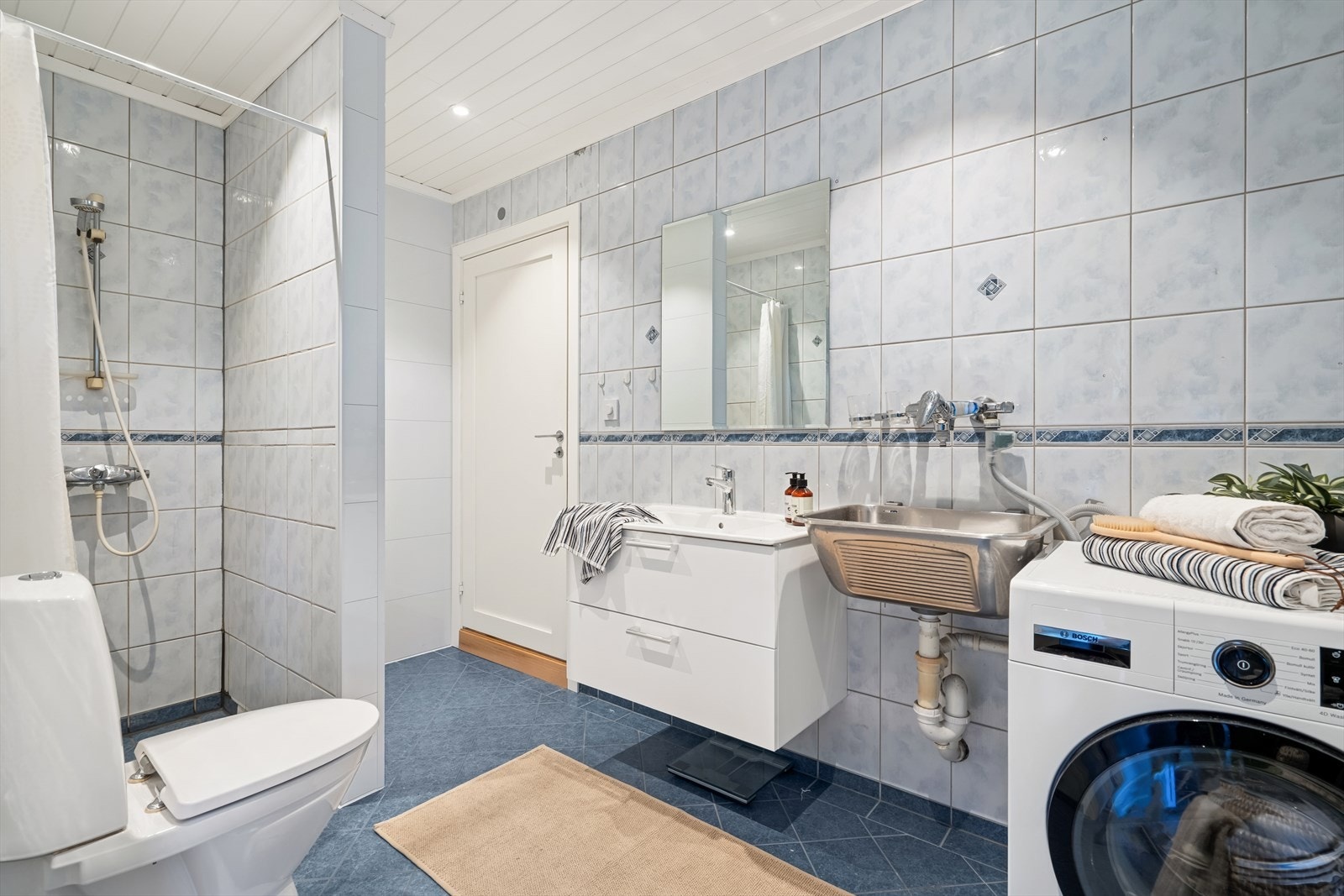 Utstyrt med dusjhjørne, gulvstående toalett, opplegg for vaskemaskin og moderne baderomsinnredning. Galleribilde