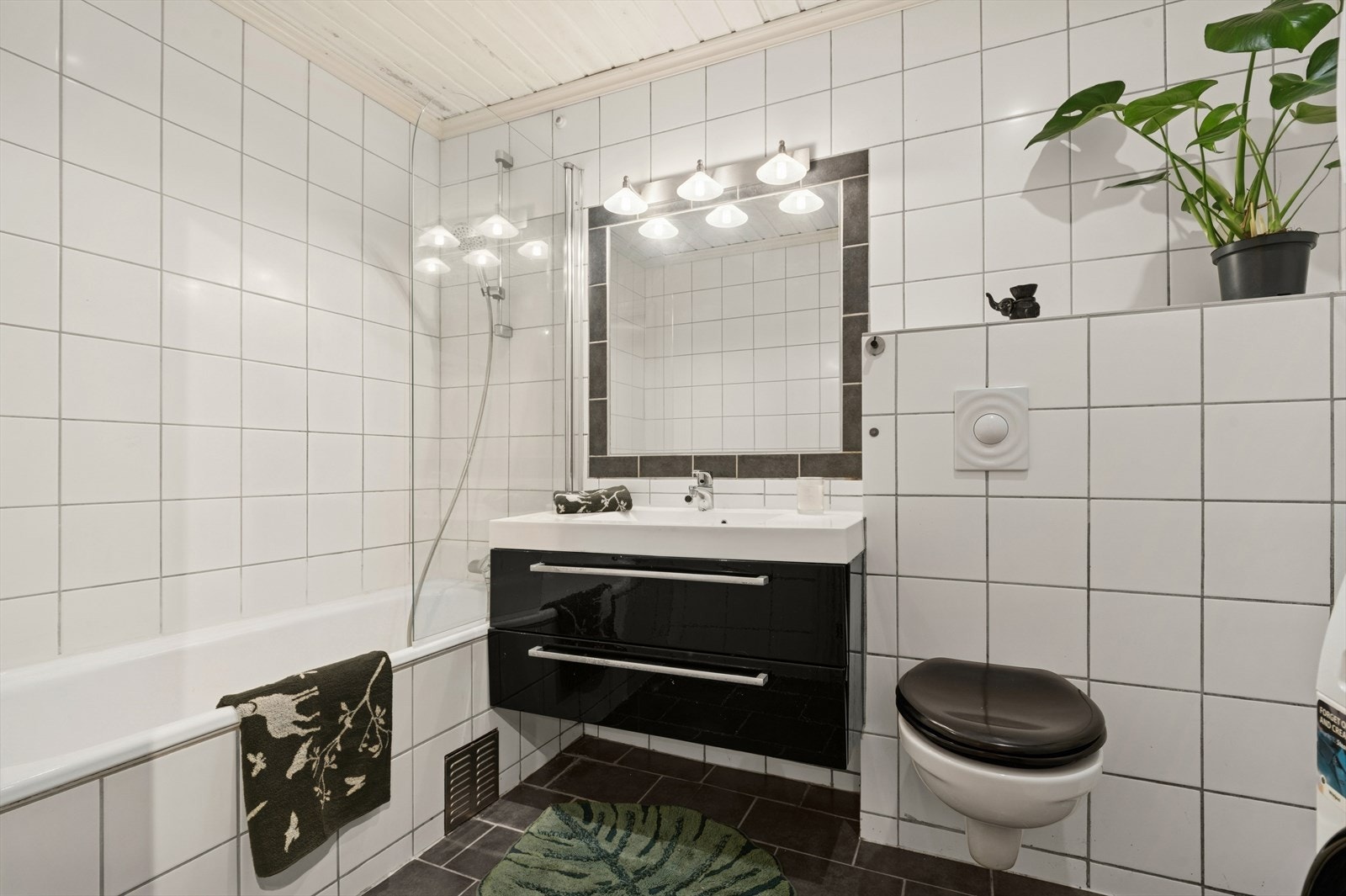 Baderomsinnredning med glatte fronter i høyglanset utførelse. Speil over servant. Dusj i badekar, servant i helstøpt plate, veggfestet klosett med innebygget sisterne og opplegg for vaskemaskin. Galleribilde