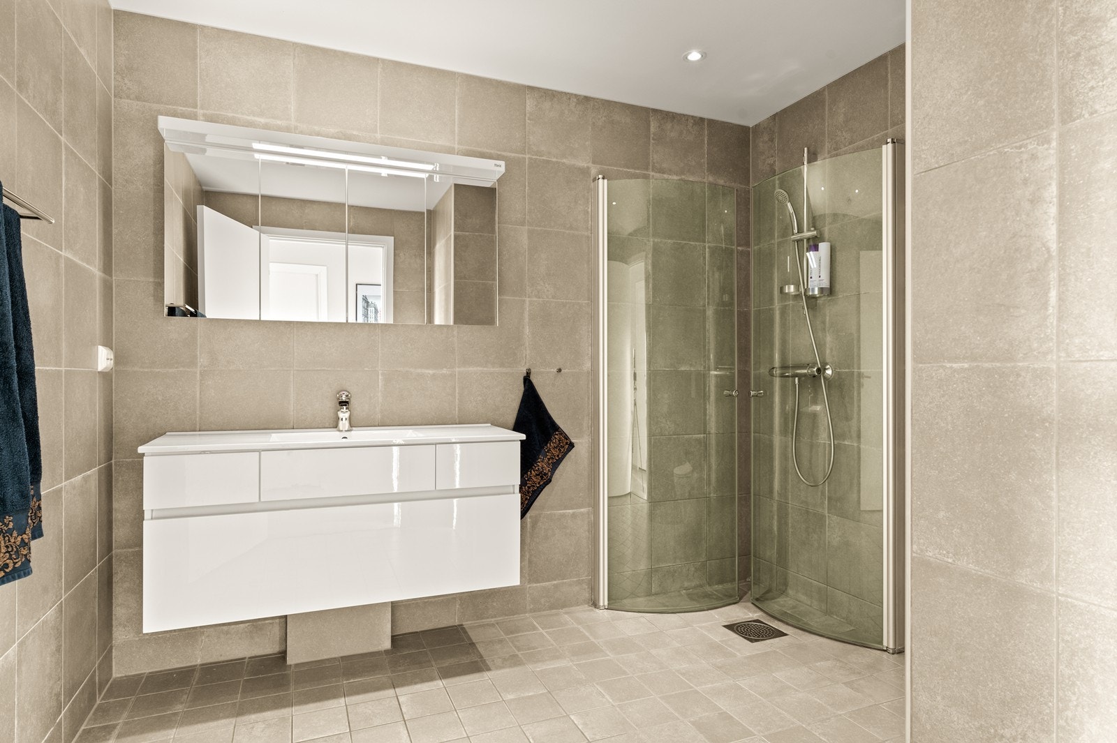 Badet har flislagte overflater og er utstyrt med servantmøbel og speilskap med belysning. Galleribilde