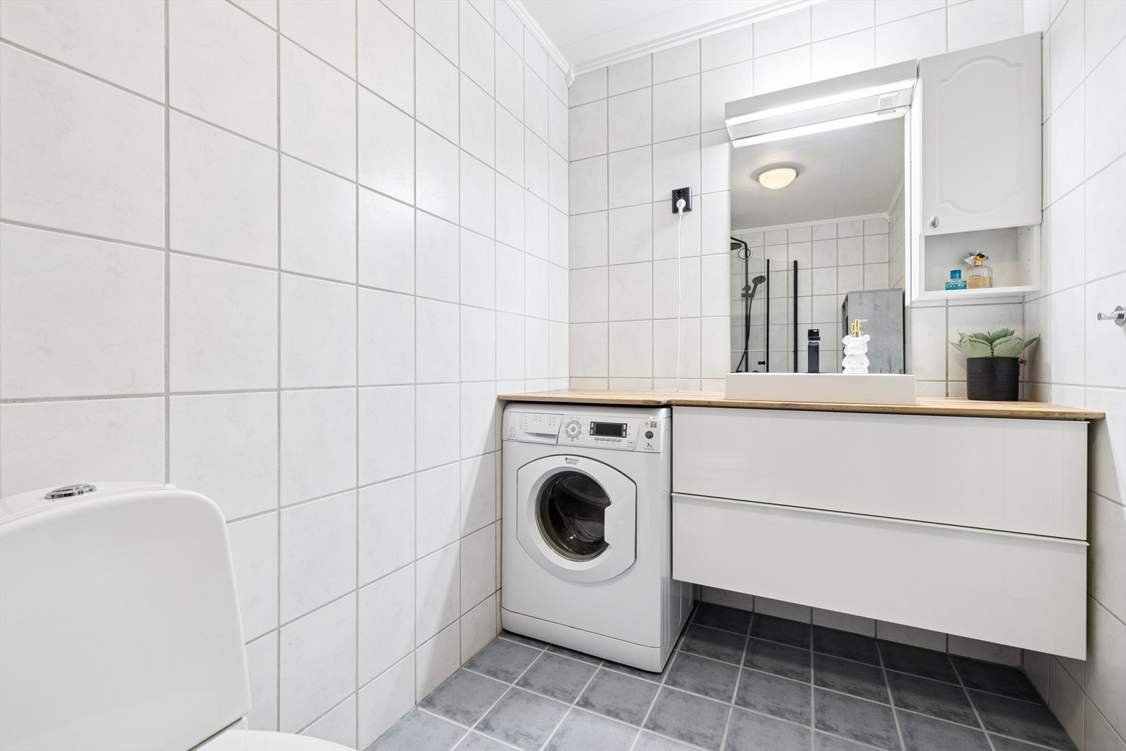 Rommet er innredet med baderomsinnredning med skap og servant, bred benkeplate med gode arbeidsforhold, toalett, opplegg for vaskemaskin og dusjkar med glassvegger. Galleribilde