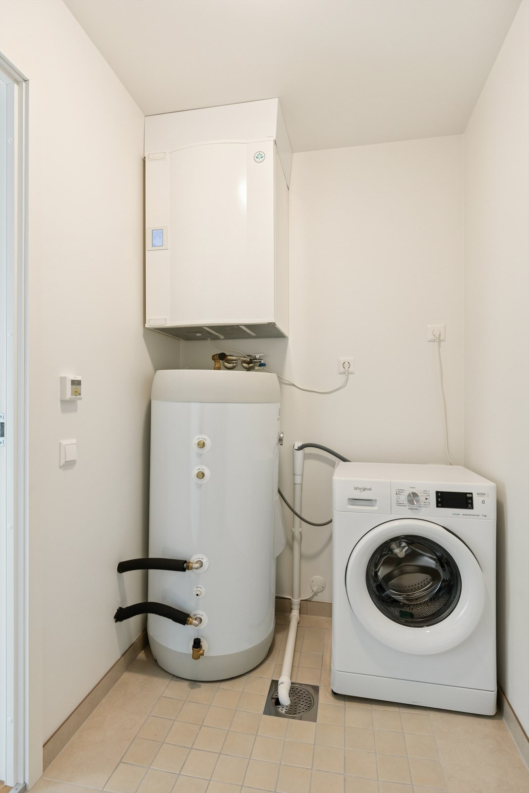 Praktisk vaskerom med fliser på gulv og opplegg til vaskemaskin. Her er også varmtvannstank og motor til balansert ventilasjon. Galleribilde