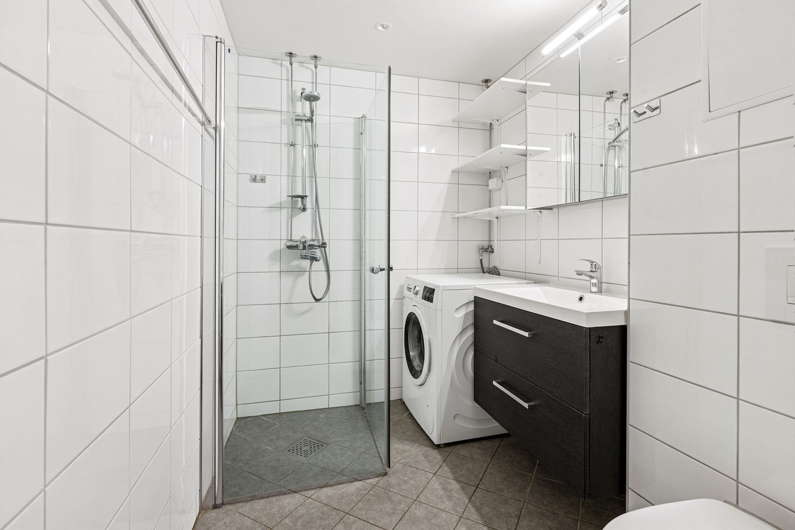 Badet har dusj med innfellbare dusjvegger, vegghengt toalett og moderne innredning. Plass til vaskemaskin Galleribilde