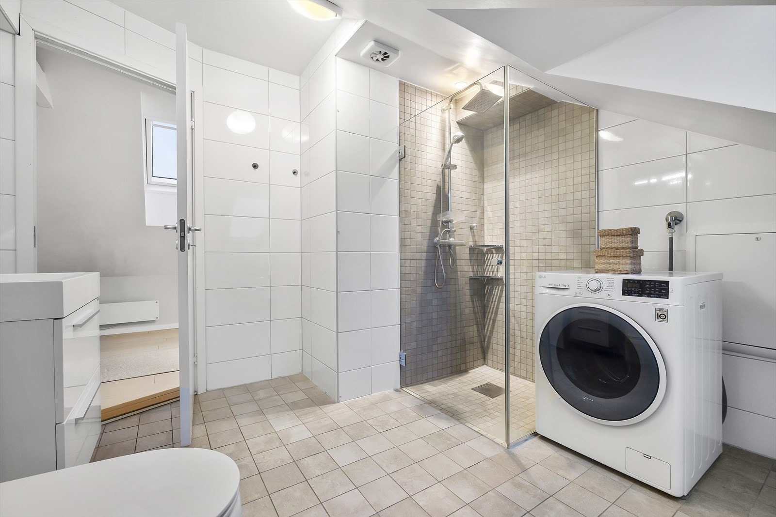 Flislagt bad med dusjhjørne, innredning og opplegg for vaskemaskin. Galleribilde