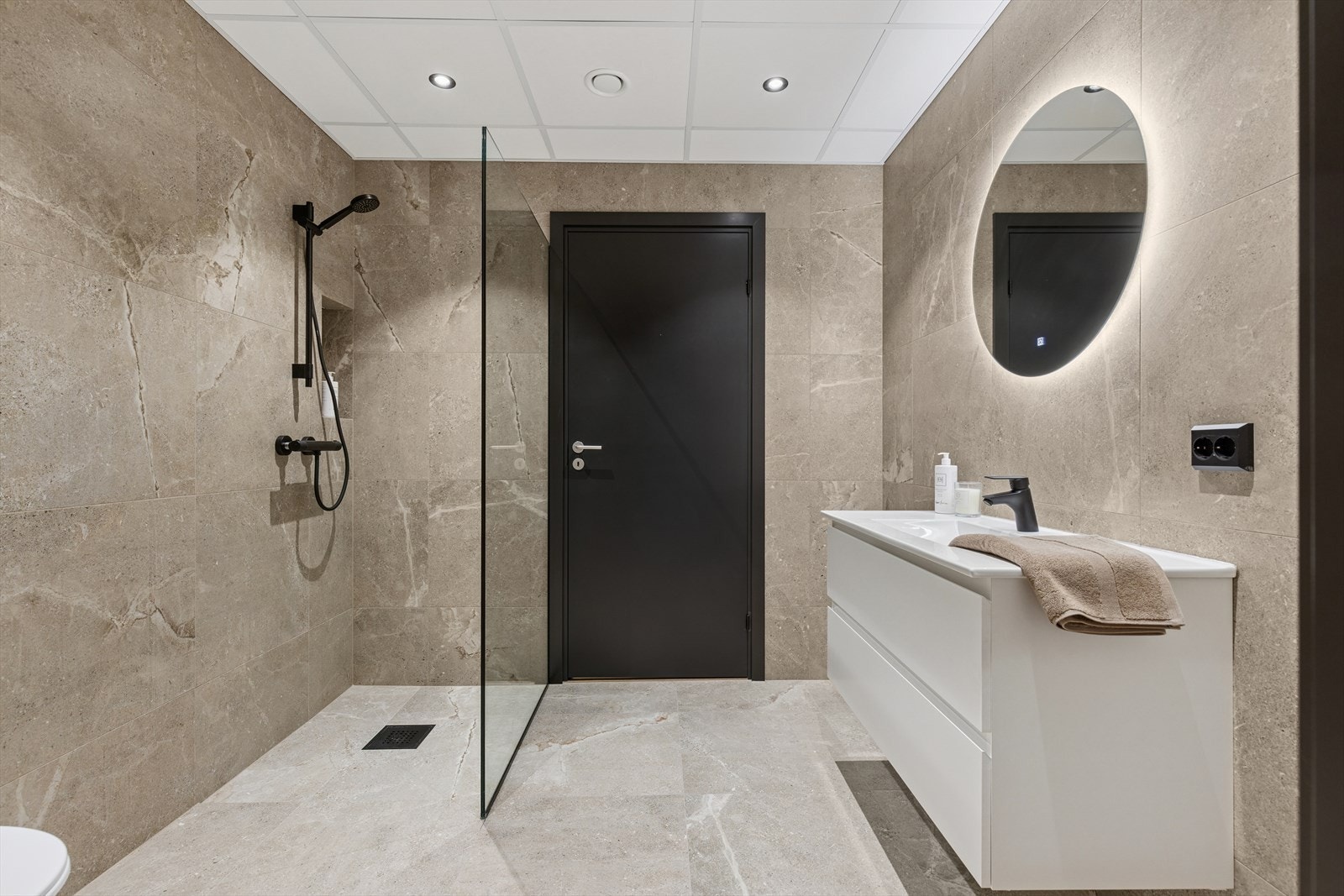 Flott innredning med skuffer og overliggende servant. Lyssatt vegghent speil. Dusjhjørne med glasvegg og armaturer i sort utførelse. Vegghengt toalett. Galleribilde